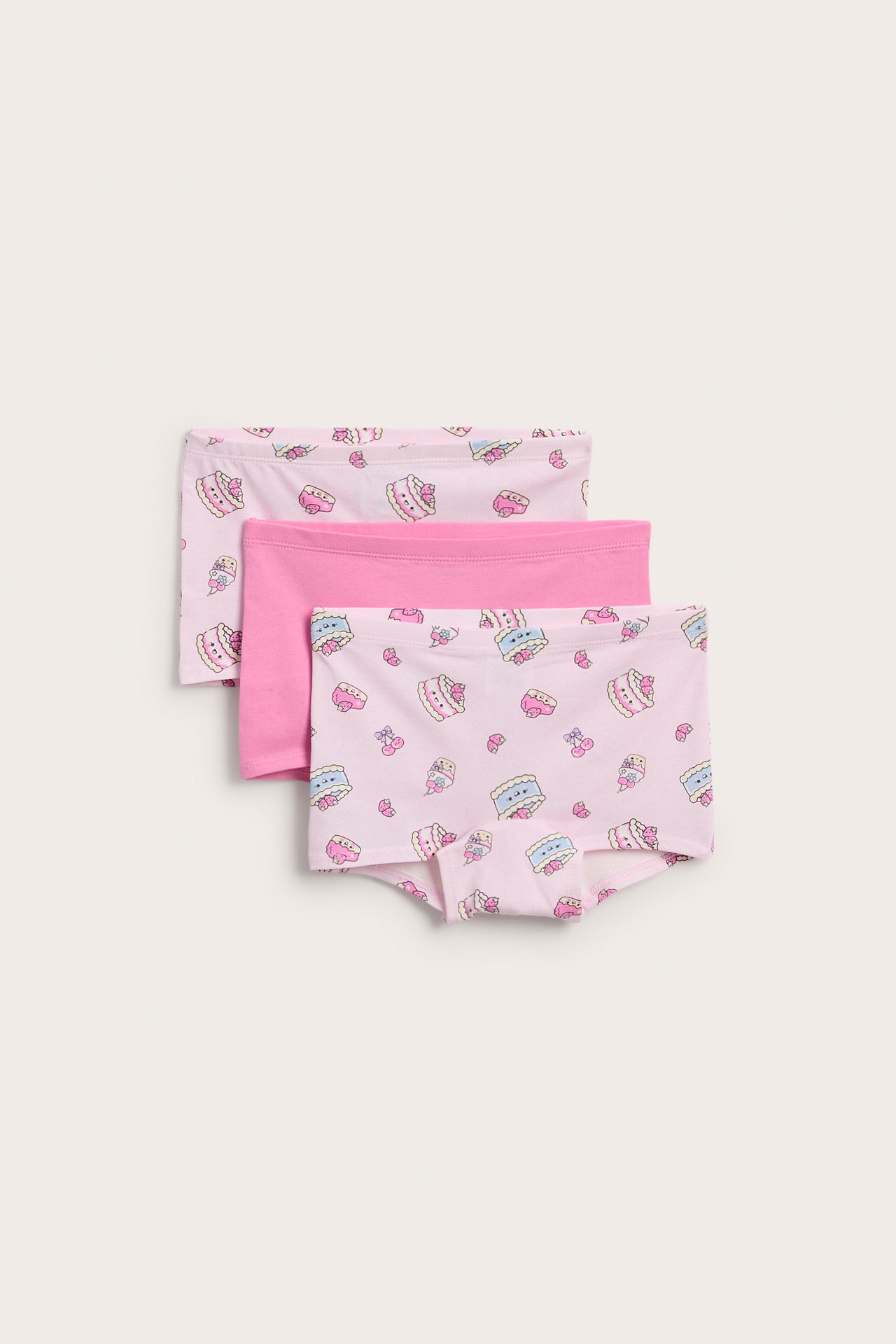 Edestä pinkit lasten bokserit cupcake-kuviolla, pinottuna kahden muun pinkin parin kanssa.