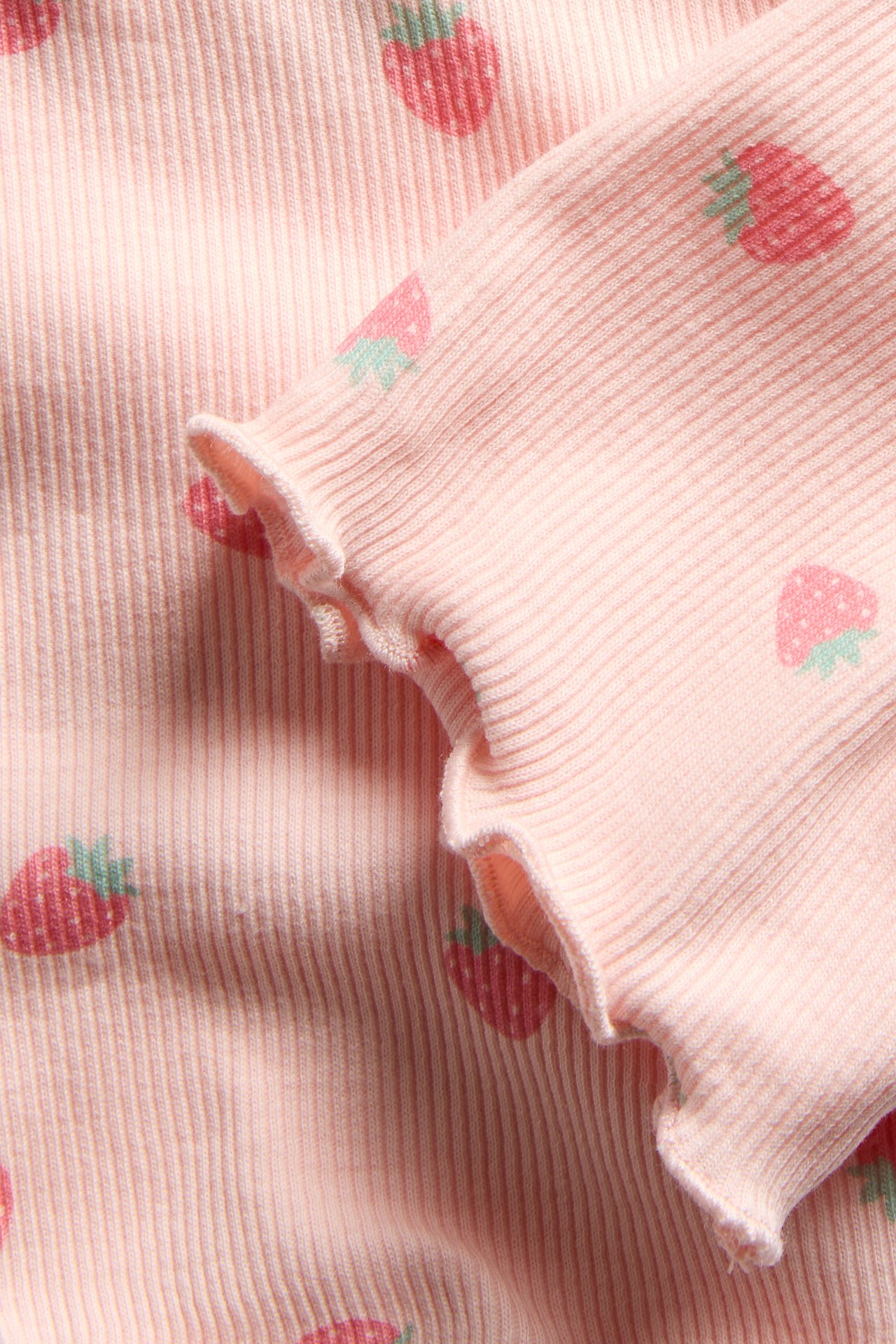 Zbliżenie jasnoróżowego prążkowanego materiału w truskawki z falbanowymi brzegami.