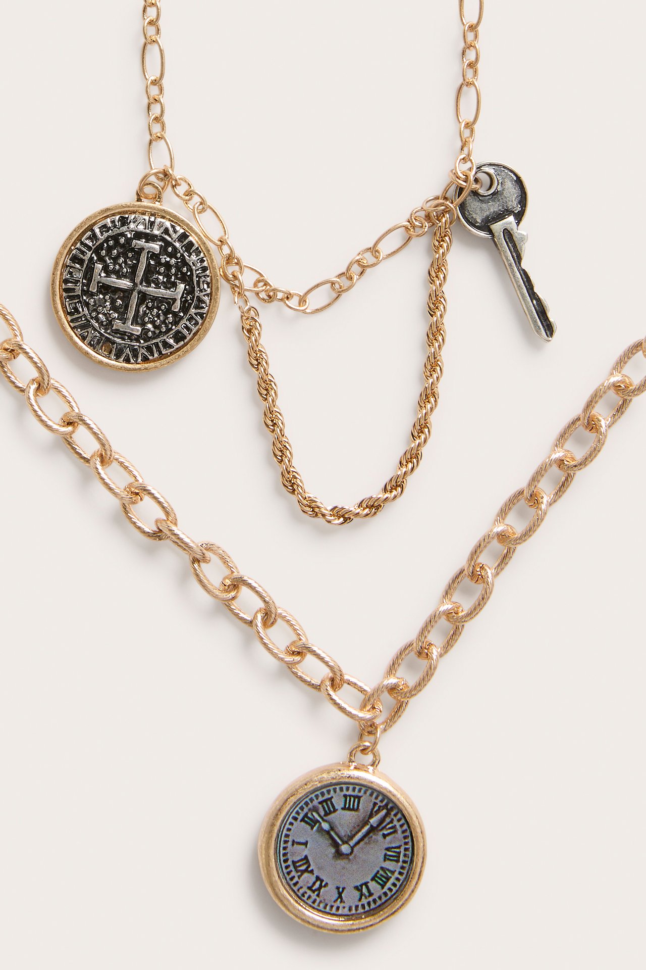 Närbild på ett lagerhalsband i guldfärg med klock-, mynt- och nyckelberlocker.