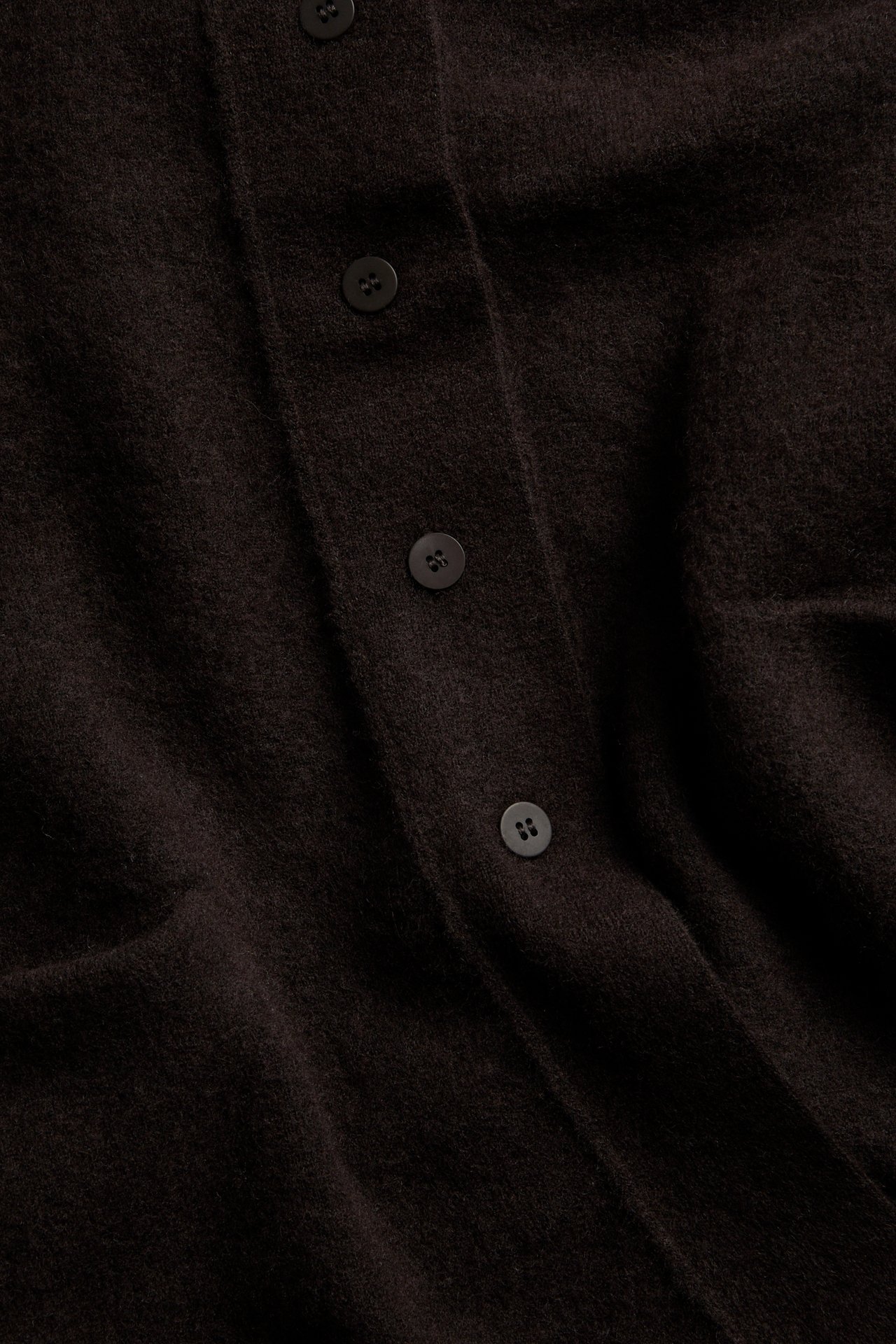 Nærbilde av mørkebrun strikket cardigan med knapper.