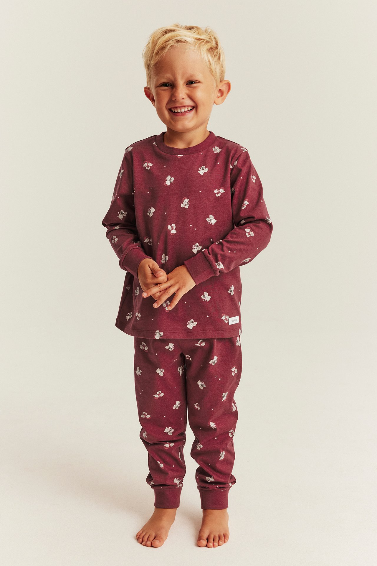 Edestä, lapsi päällä viininpunainen kuvioitu pitkähihainen pyjama, jossa valkoinen eläinkuvio.