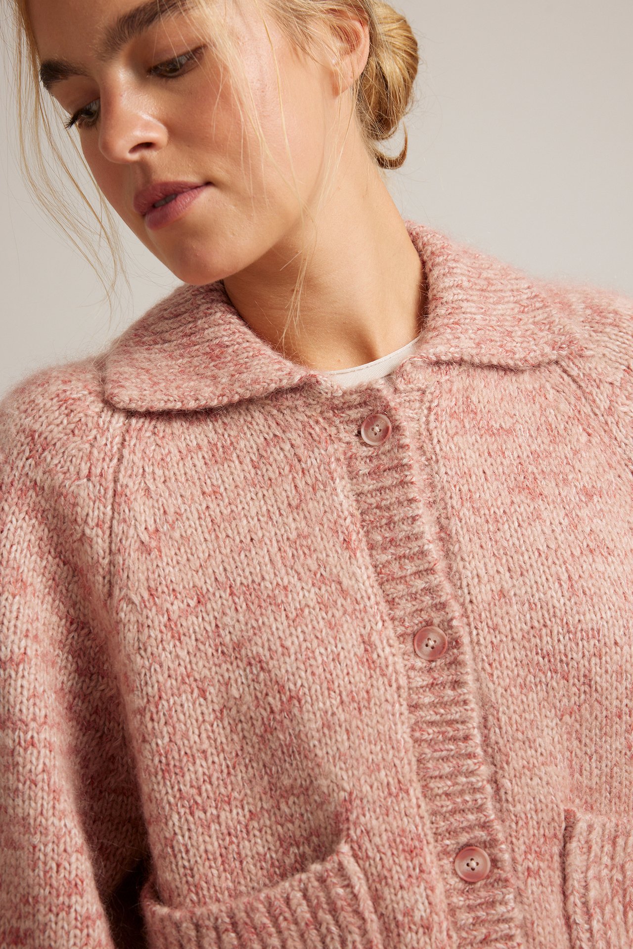 Närbild framifrån: Kvinna i rosa spräcklig stickad kofta över en vit t-shirt.