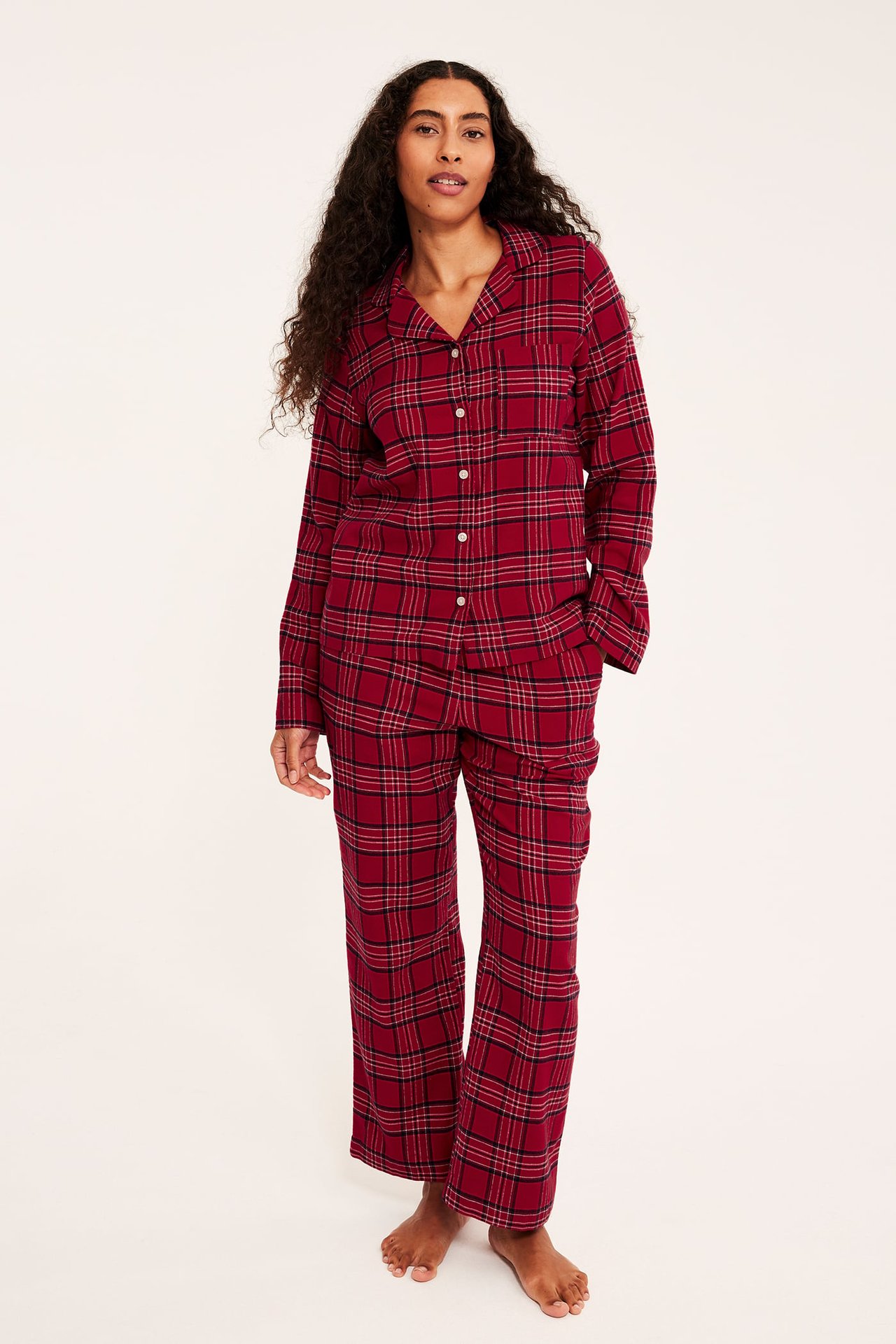 Edestä kuvattu nainen punaisessa ruudullisessa pyjamasetissä, jossa paita ja housut.