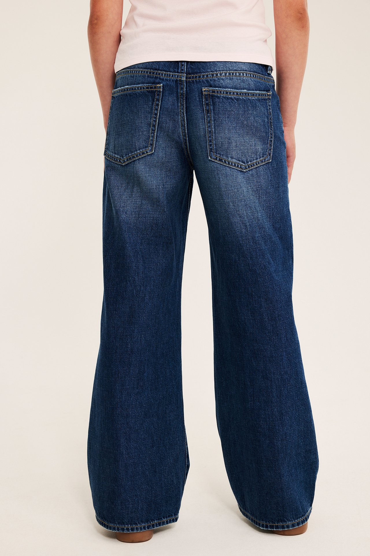 Bakfra: voksen person med mørkeblå wide-leg jeans og en lyserosa t-skjorte.