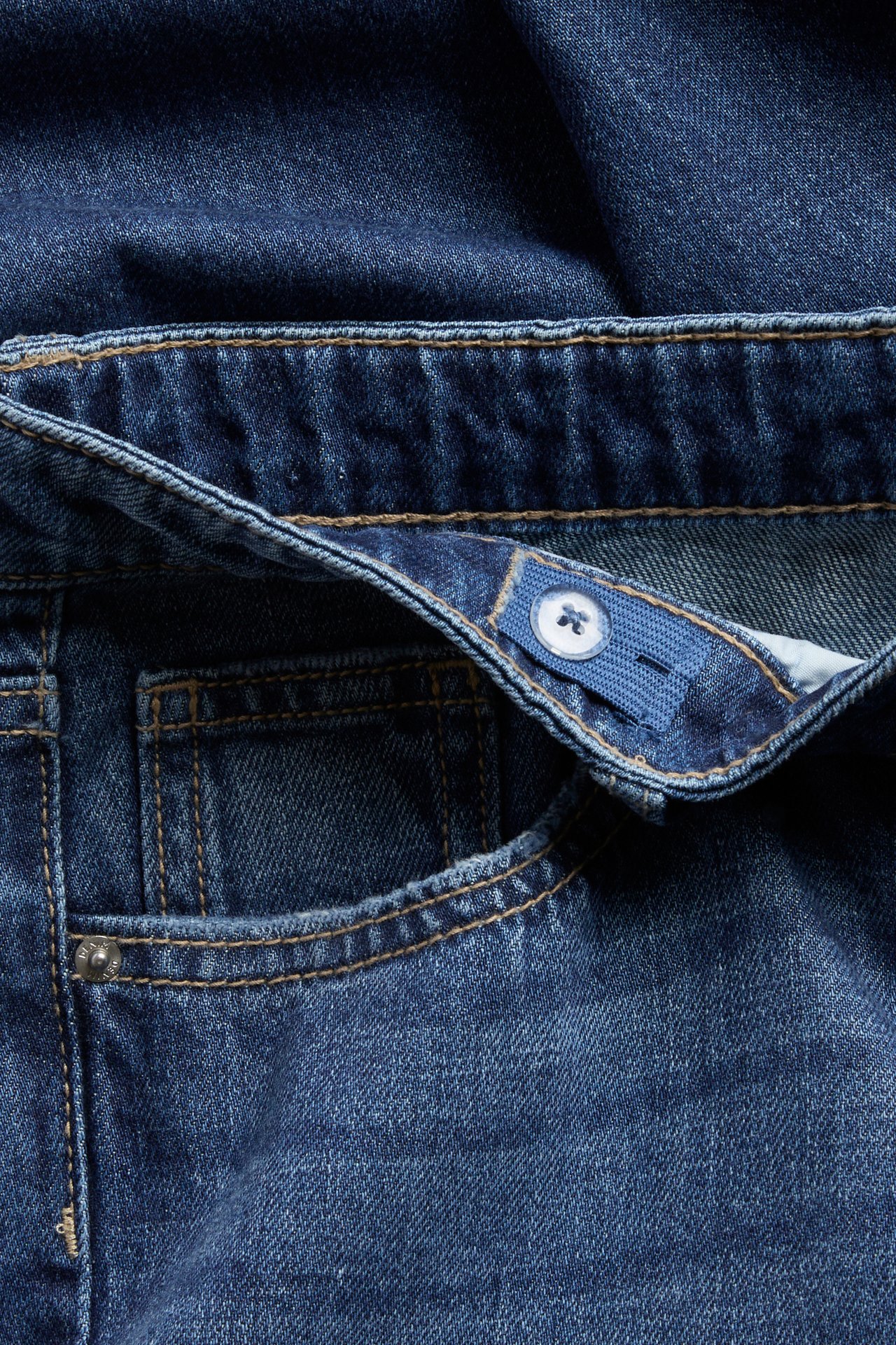 Närbild av blå denimjeans med framficka och justerbart resårband med knapp i midjan.