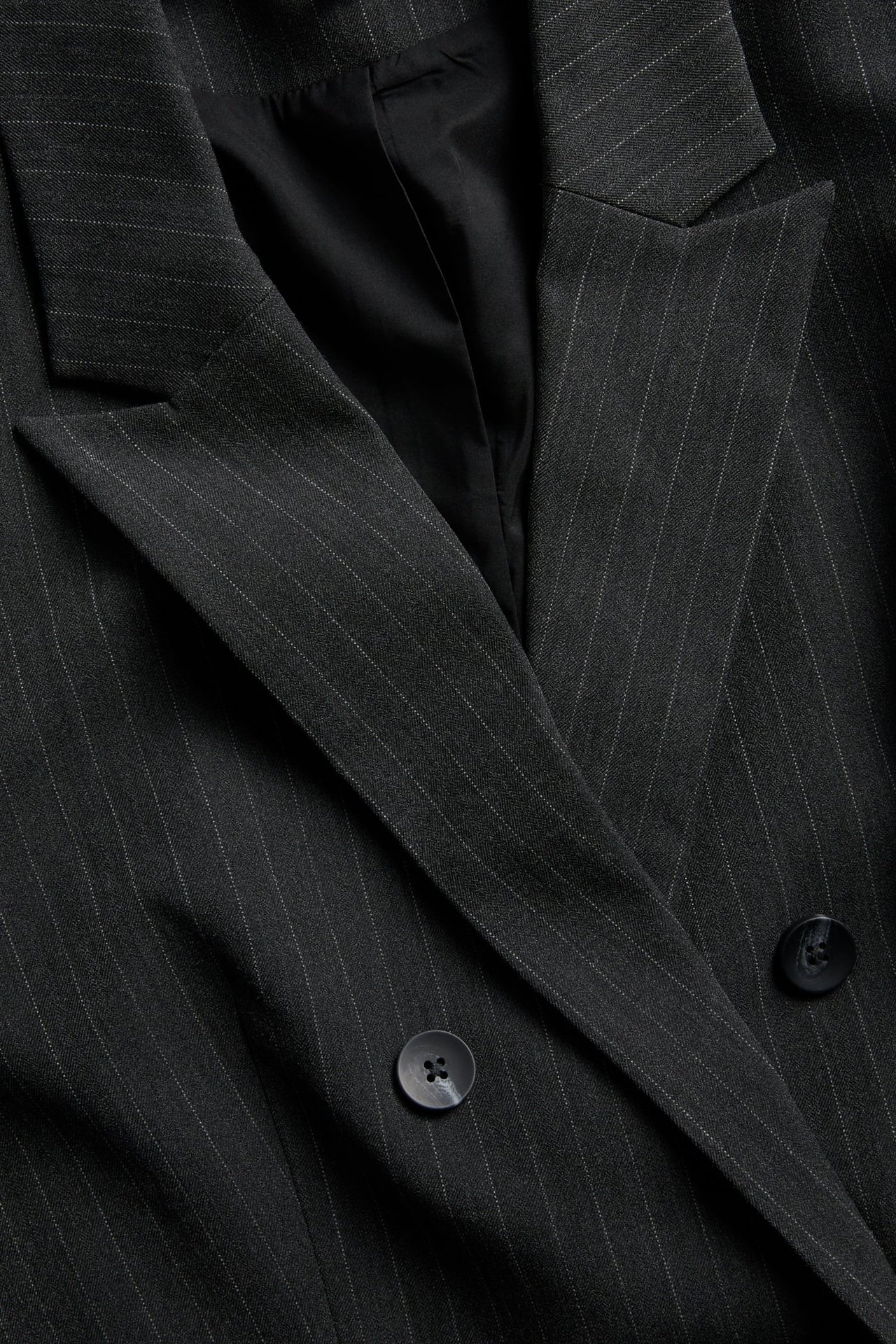 Nærbilde av en mørkegrå nålestripet dobbeltspent blazer med to svarte knapper.