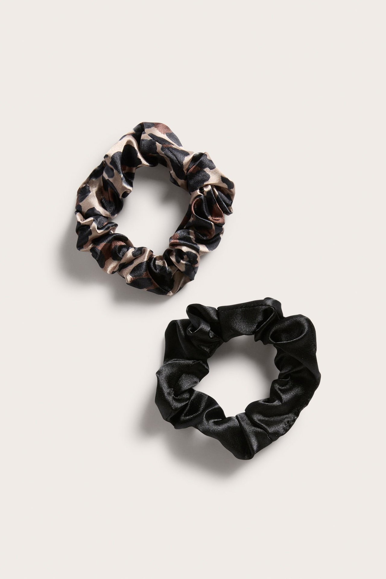 Nærbilde av en 2-pakning sateng scrunchies: en med dyremønster og en ensfarget svart.