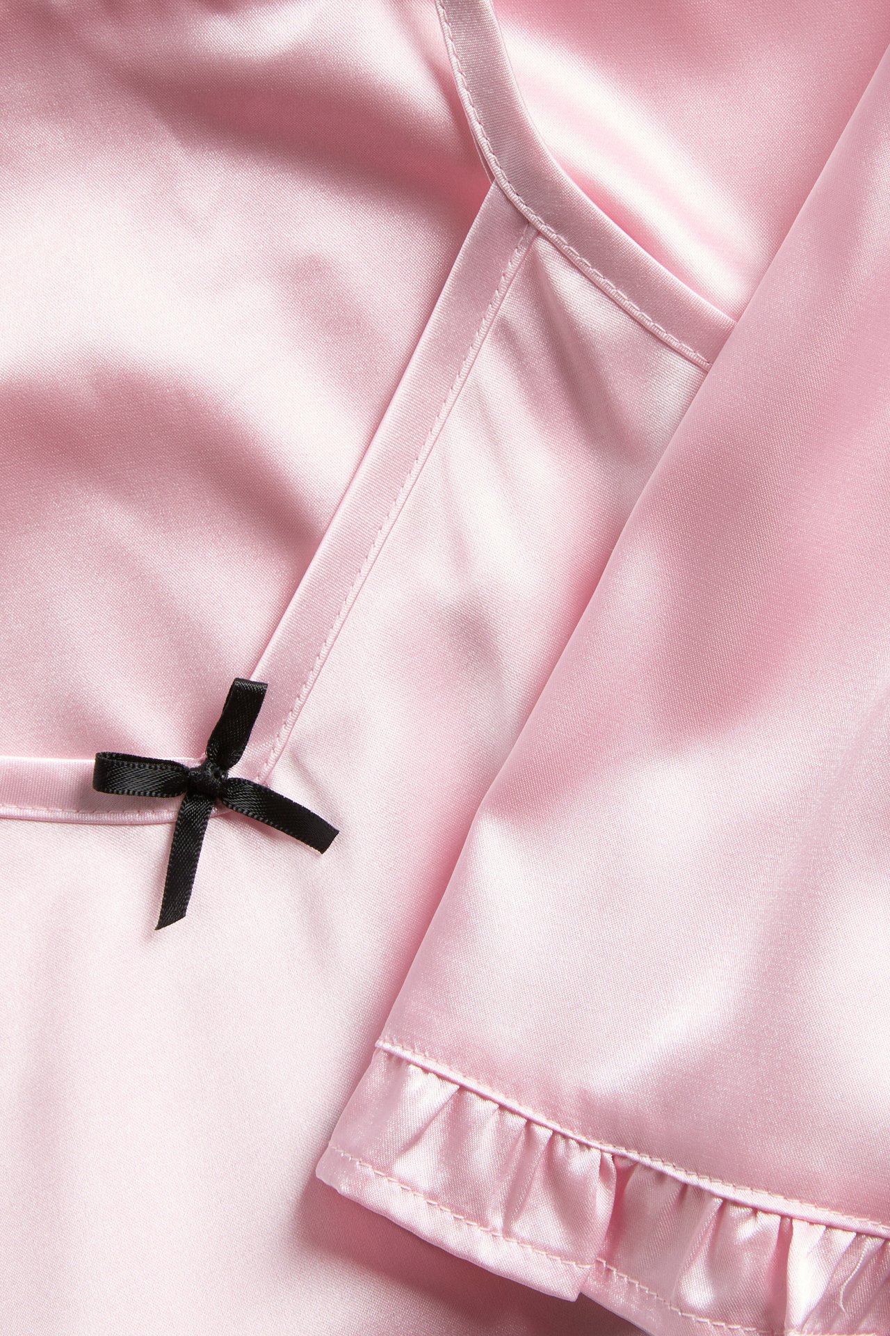 Närbild av rosa satinpyjamas med svart rosett och volangkant.