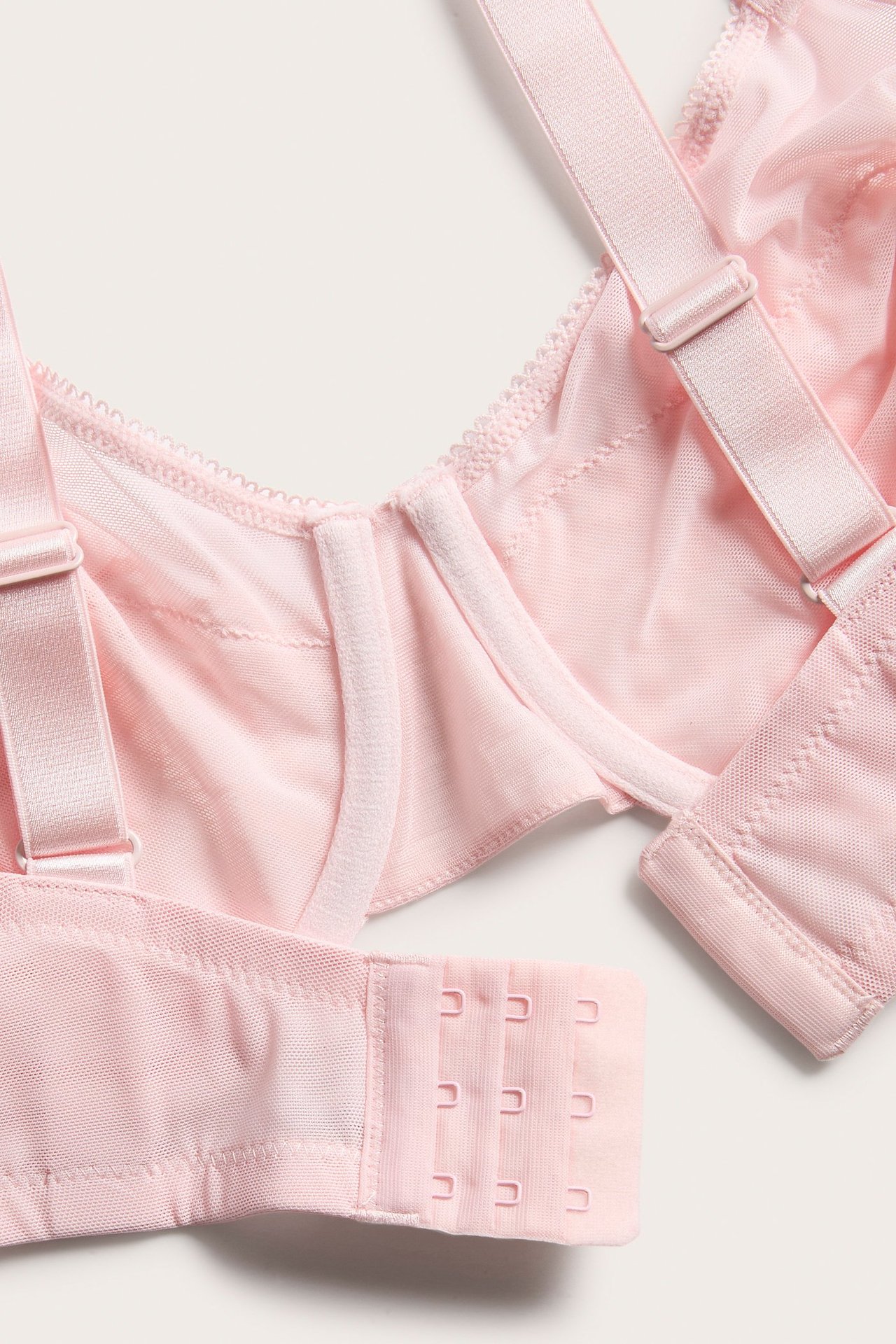 Närbild på en rosa spets-bh med bygel, justerbara axelband och hyskknäppning med två rader.