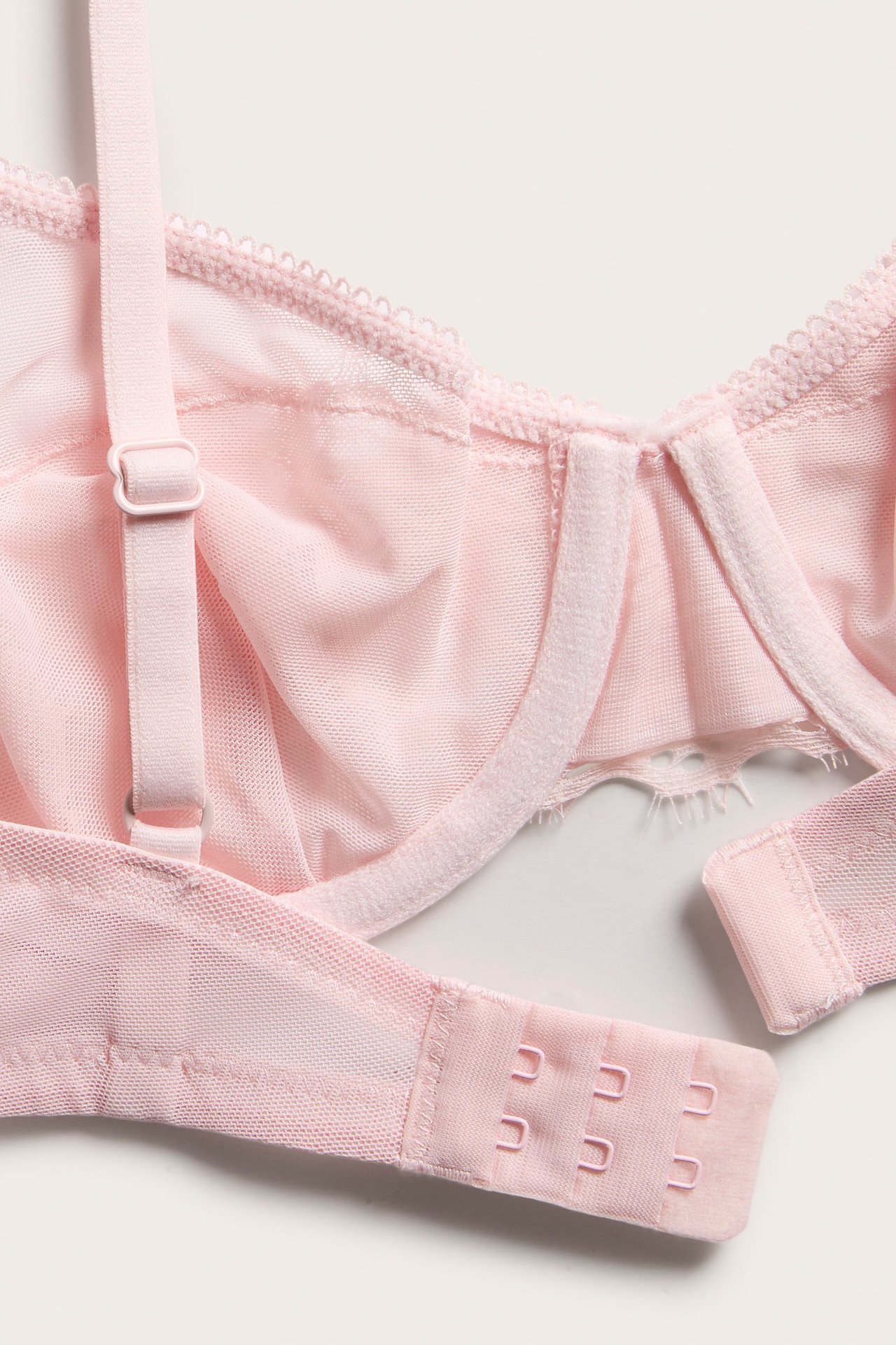 Lähikuva vaaleanpunaisista kaarituellisista pitsirintaliiveistä, joissa verkkoyksityiskohtia, säädettävät olkaimet ja takana hakakiinnitys.