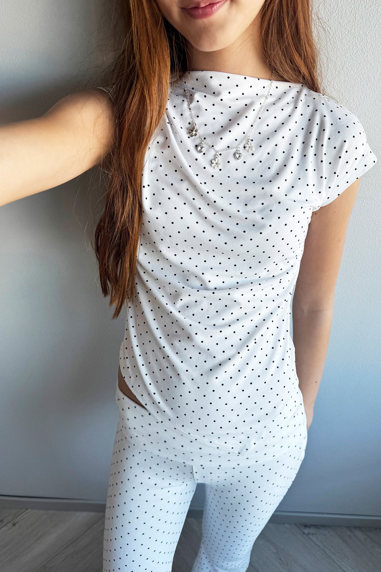Vitt prickigt tight topp med asymmetrisk nederkant, bärs av kvinna, frontvy.