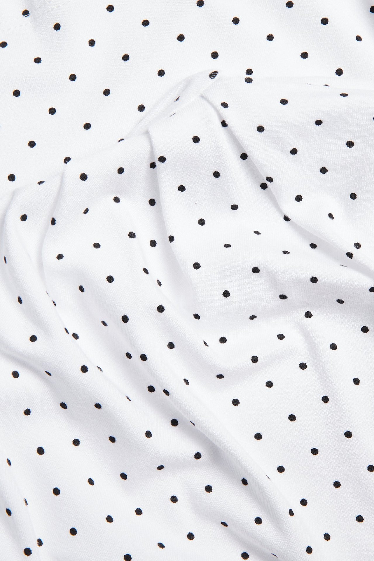 Lähikuva valkoisesta tiukasta pilkullisesta topista, jossa mustia pilkkuja ja laskostettua kangasta.