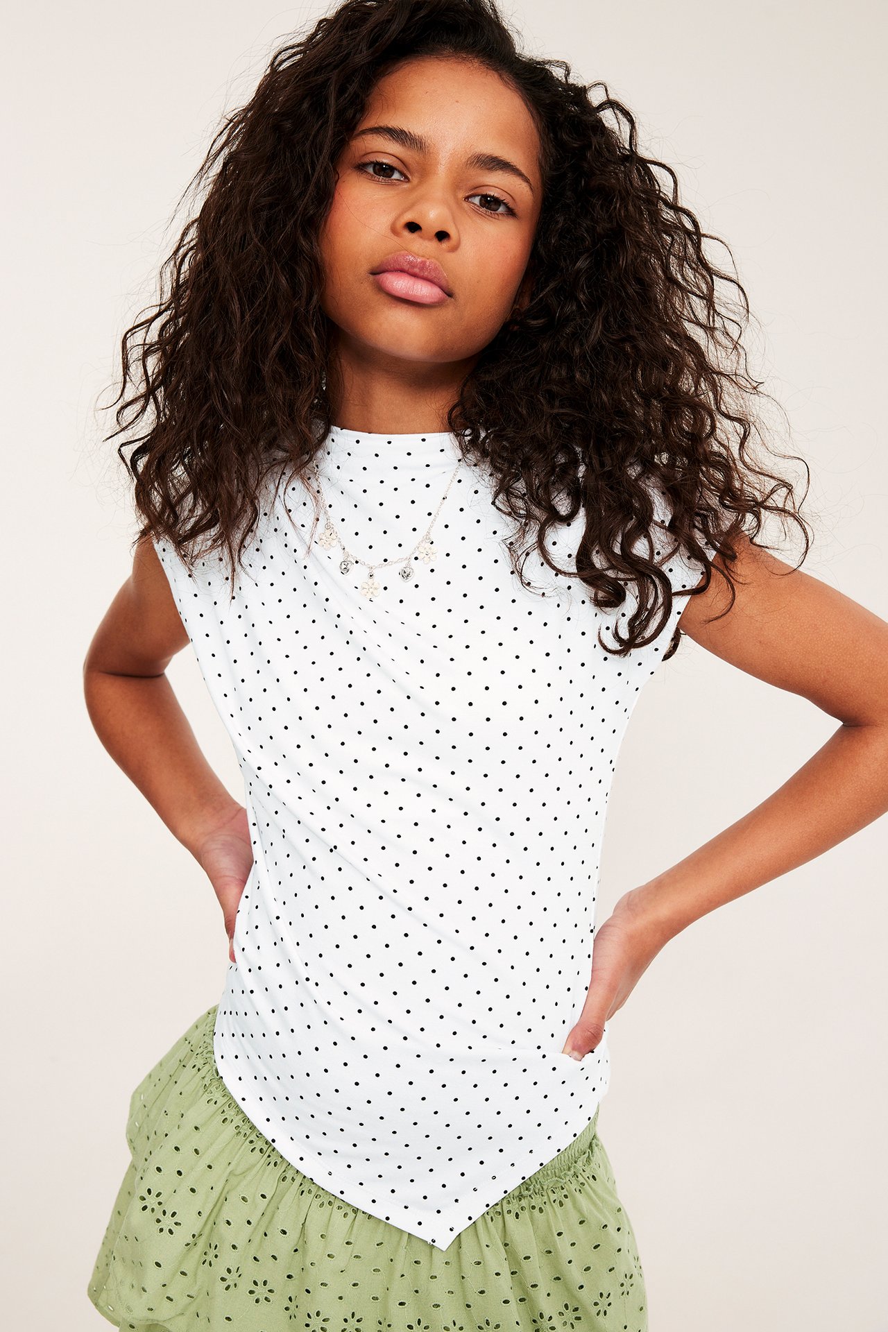 Frontbilde av barn i hvit prikkete asymmetrisk topp og grønt brodert skjørt.