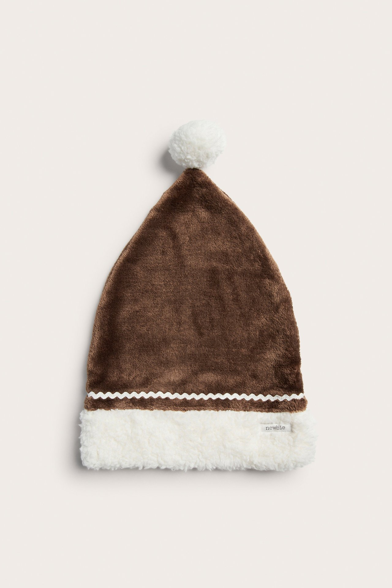 Frontvisning: Brun lodden babyhatt med hvit fuskpelskant, bølget bånd og hvit dusk.