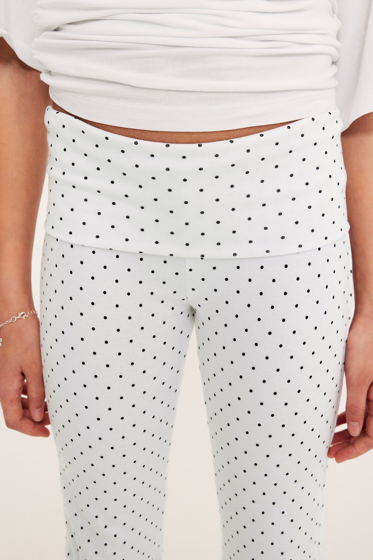 Närbild framifrån: Barn i vita prickiga utsvängda leggings med nedfällbar midja och vit topp.