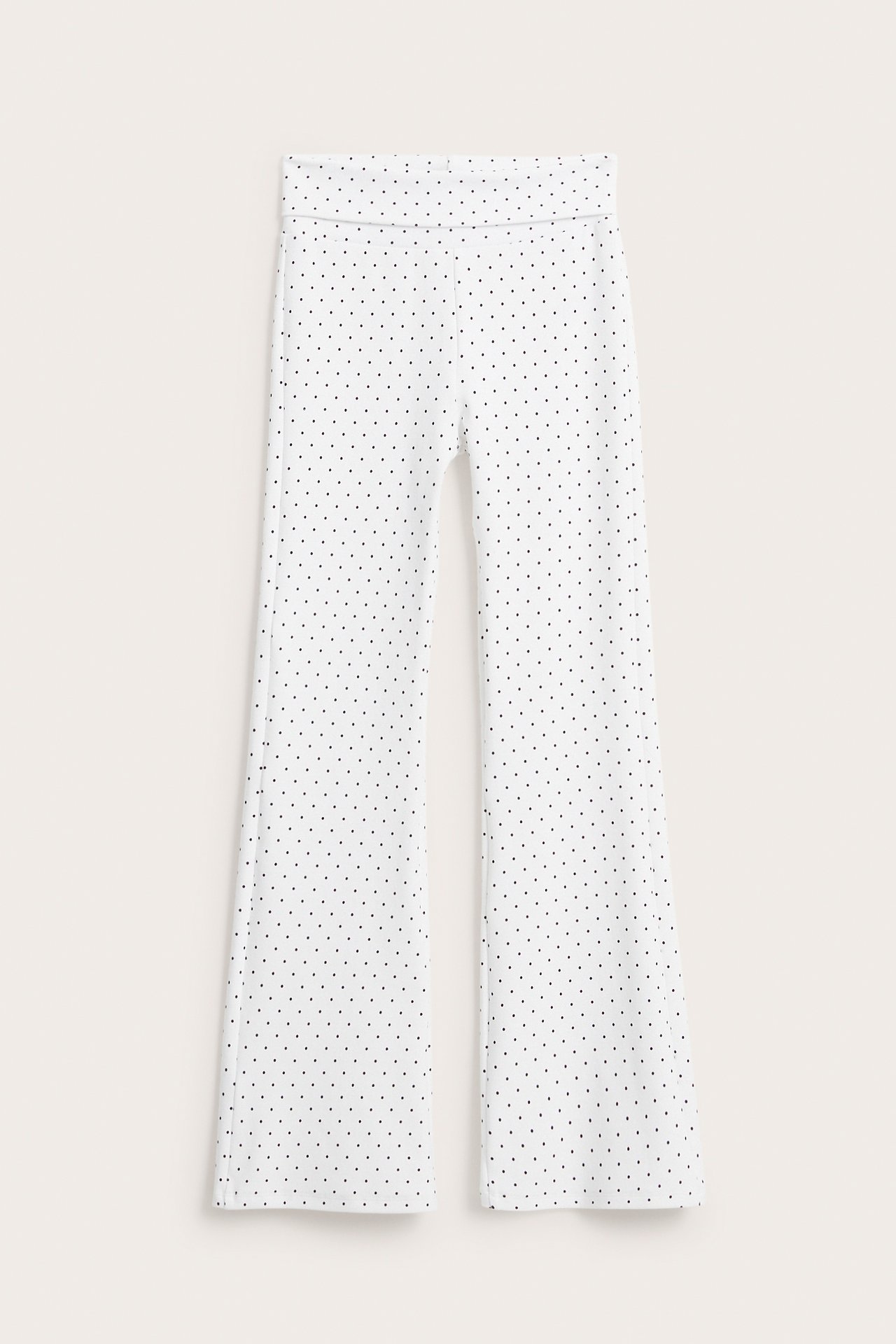 Widok z przodu: białe, rozszerzane legginsy do jogi w kropki z wywijanym pasem.