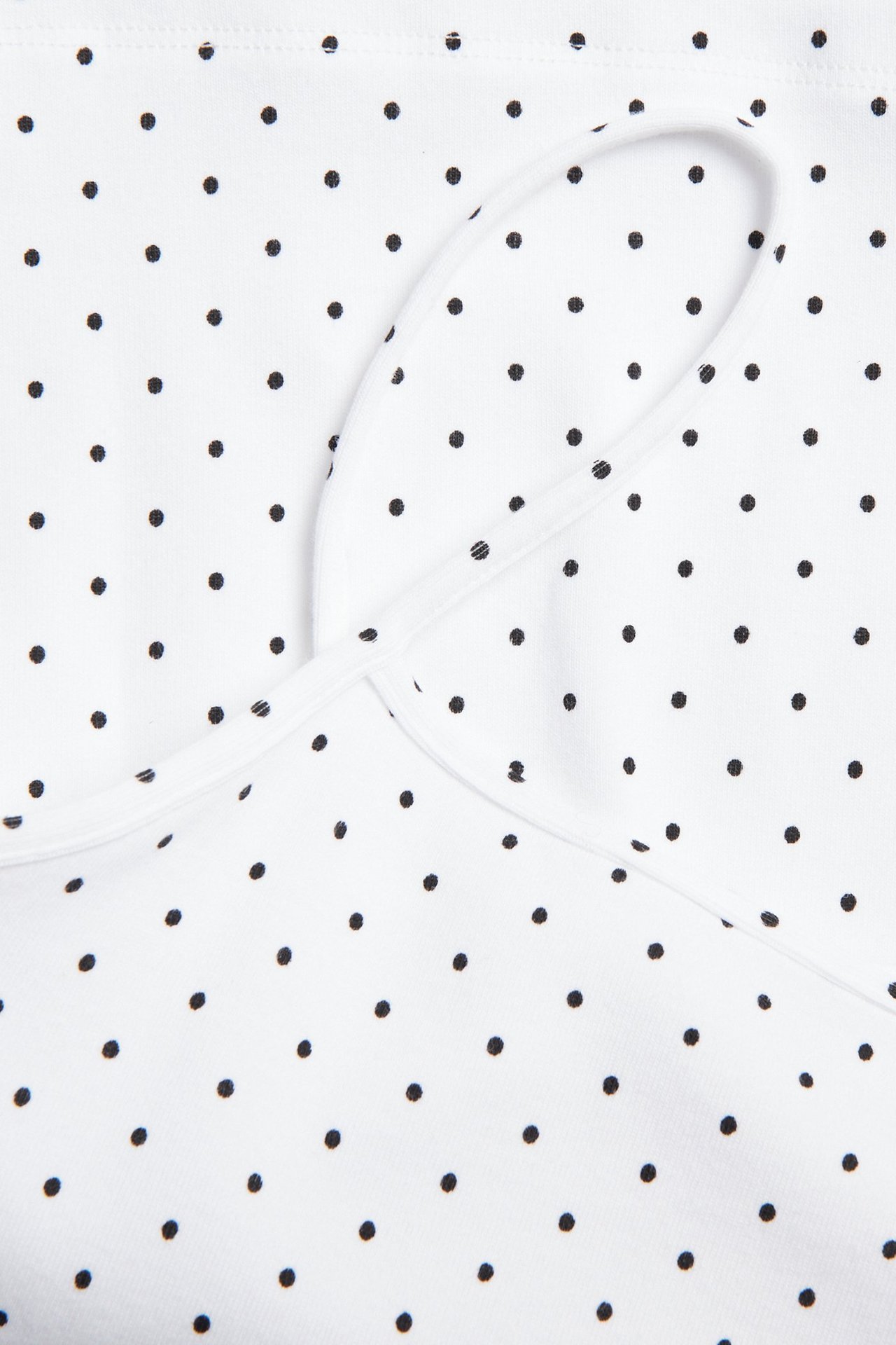 Zbliżenie na białą bawełnianą koszulkę w kropki z cienkimi ramiączkami.
