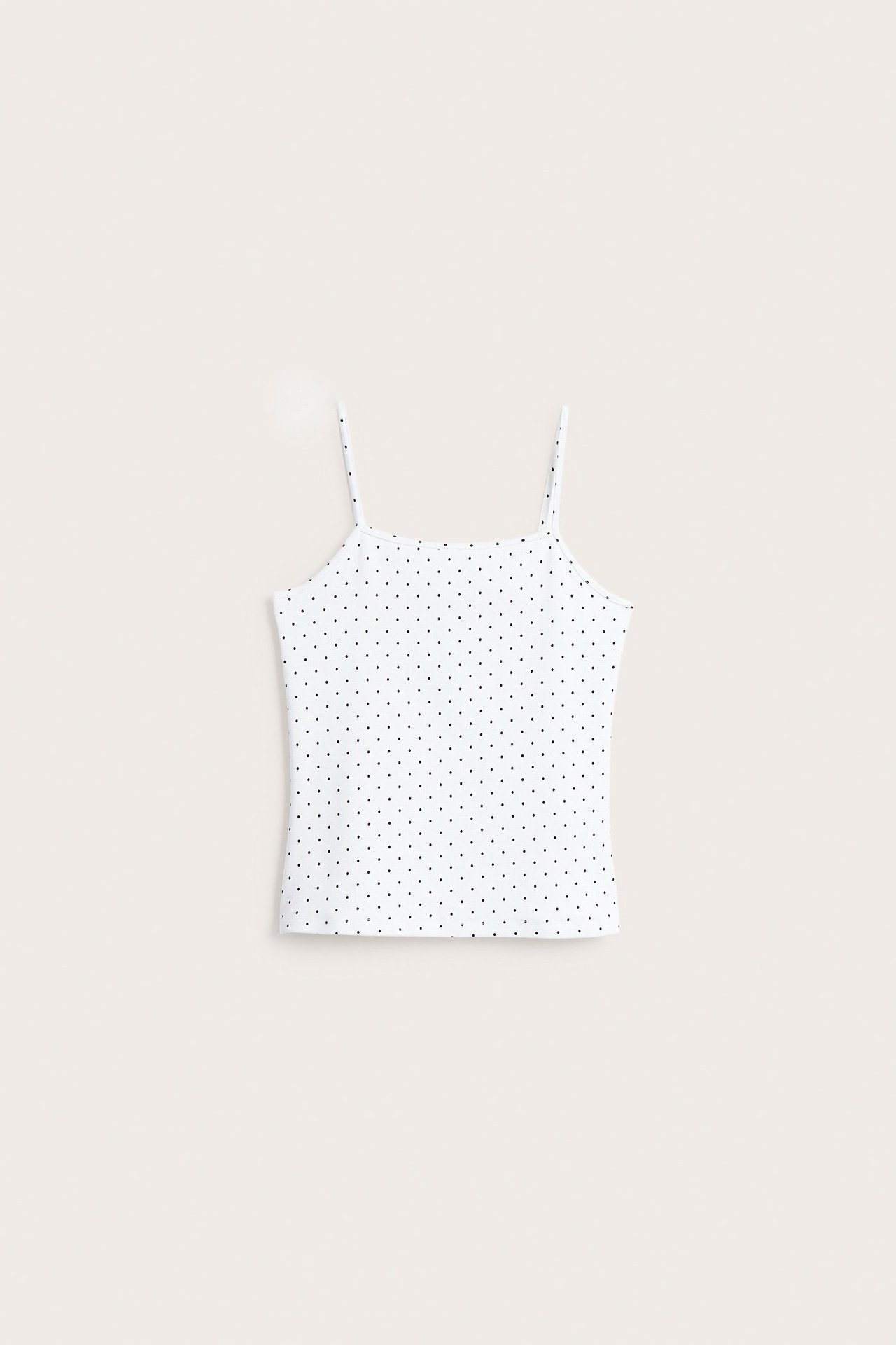 Edestäpäin valkoinen puuvillatrikooinen pilkullinen toppi ohuilla olkaimilla.