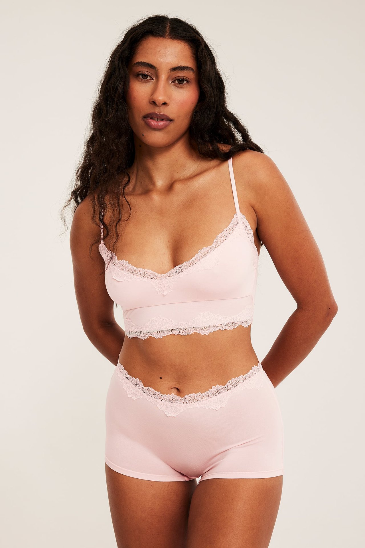 Frontvy: kvinna i ljusrosa modal spetsbralette med justerbara band och matchande spetsshorts.