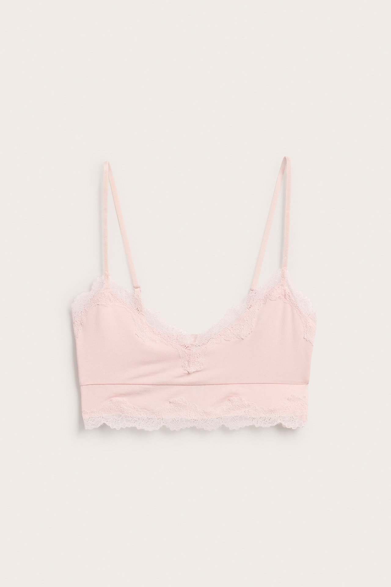 Framifrån av en ljusrosa modal spetsbralette med vita spetsdetaljer och justerbara axelband.