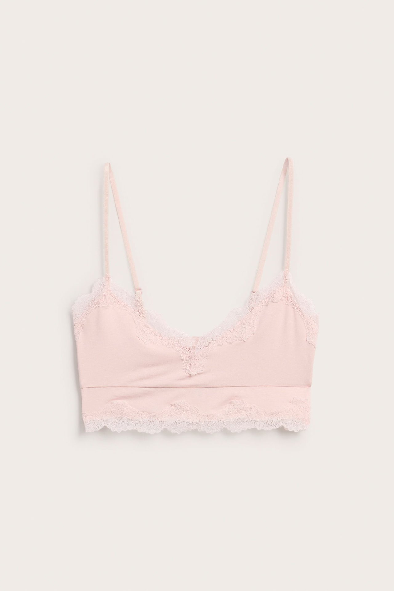 Frontbilde av en lys rosa modal bralette med hvite blondedetaljer og justerbare skulderstropper.