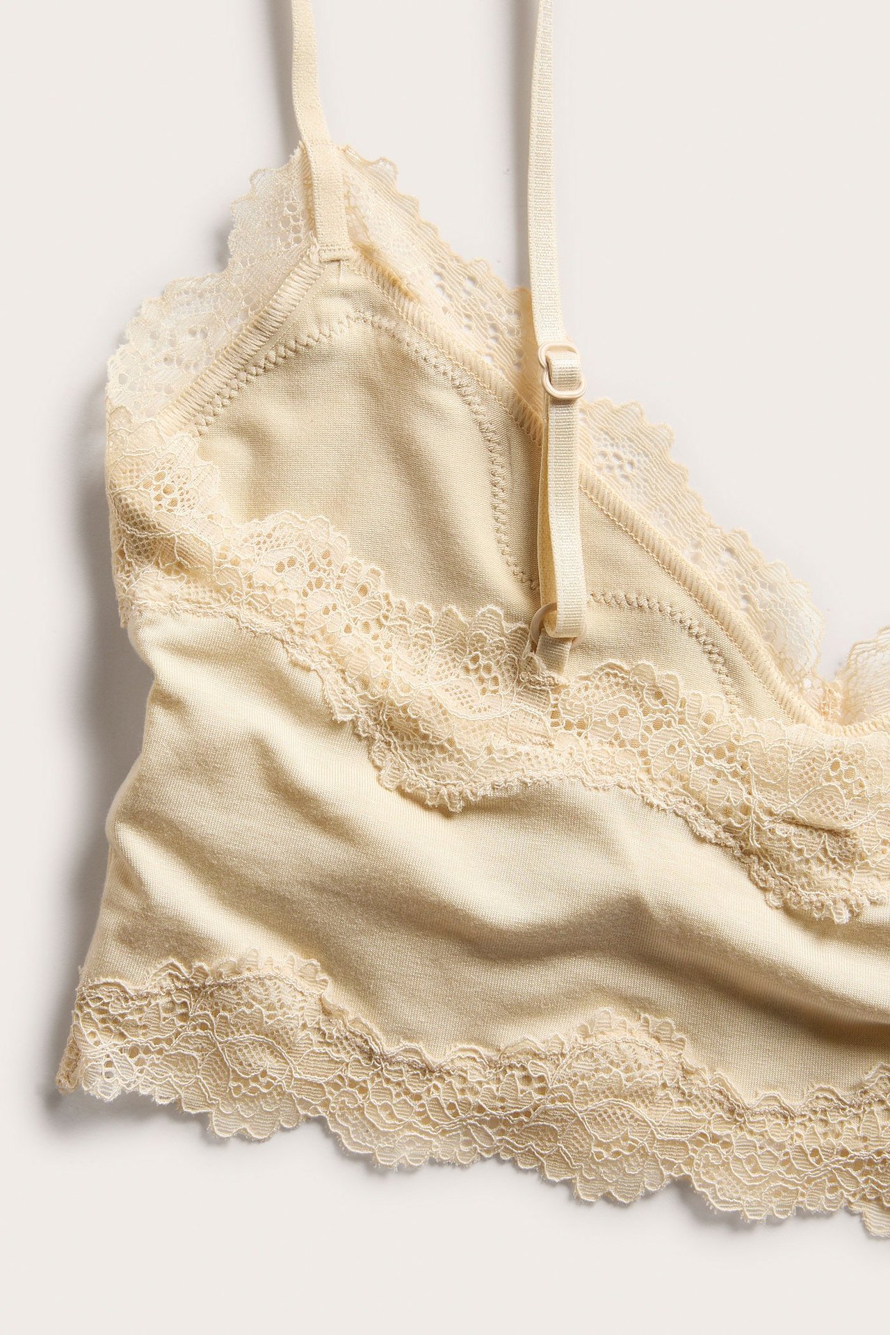 Nærbilde av en myk beige modal bralette med blondedetaljer og justerbare stropper.