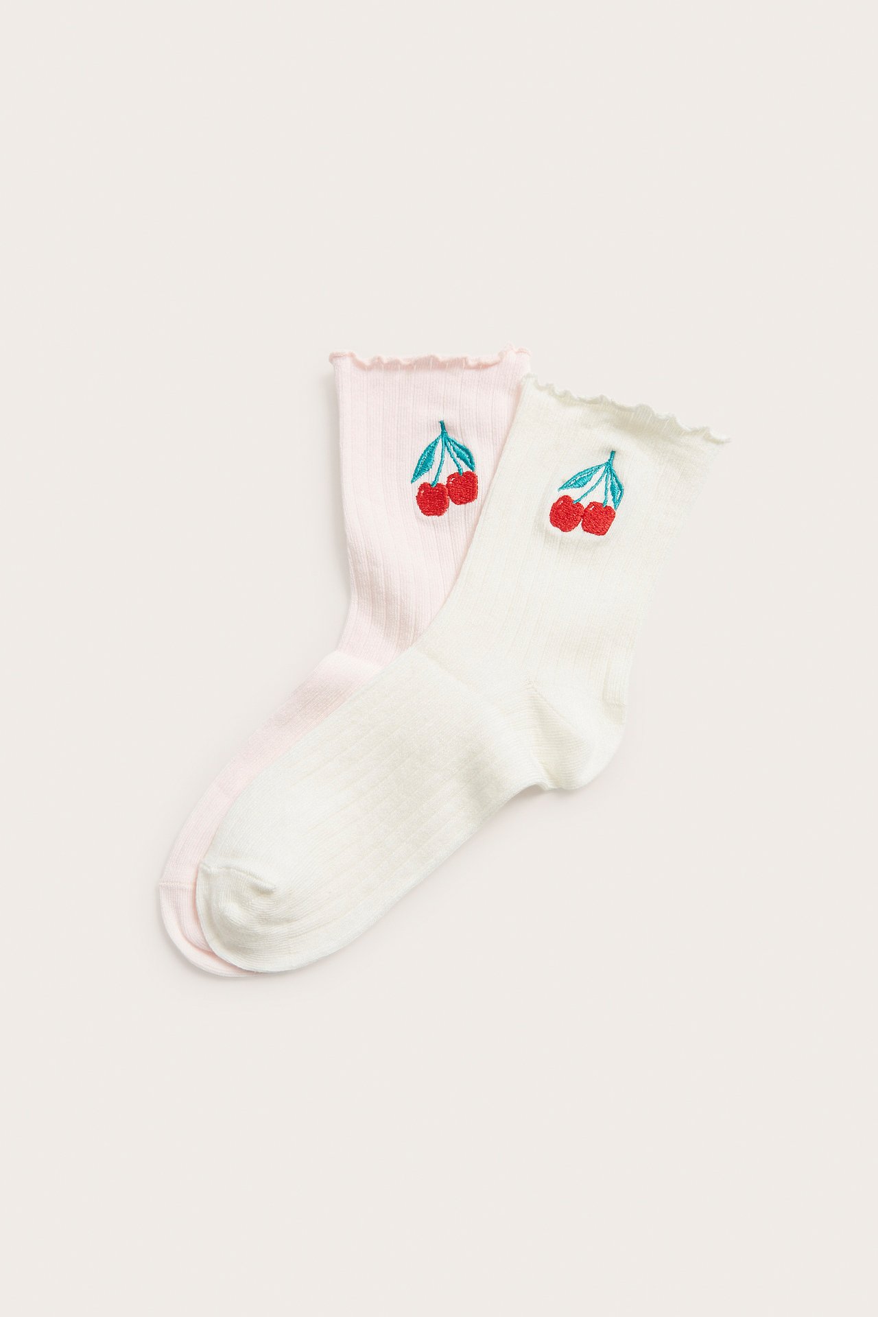 Dwie pary prążkowanych skarpetek: ecru i jasnoróżowe, z haftem czerwonych wisienek oraz falbankami.
