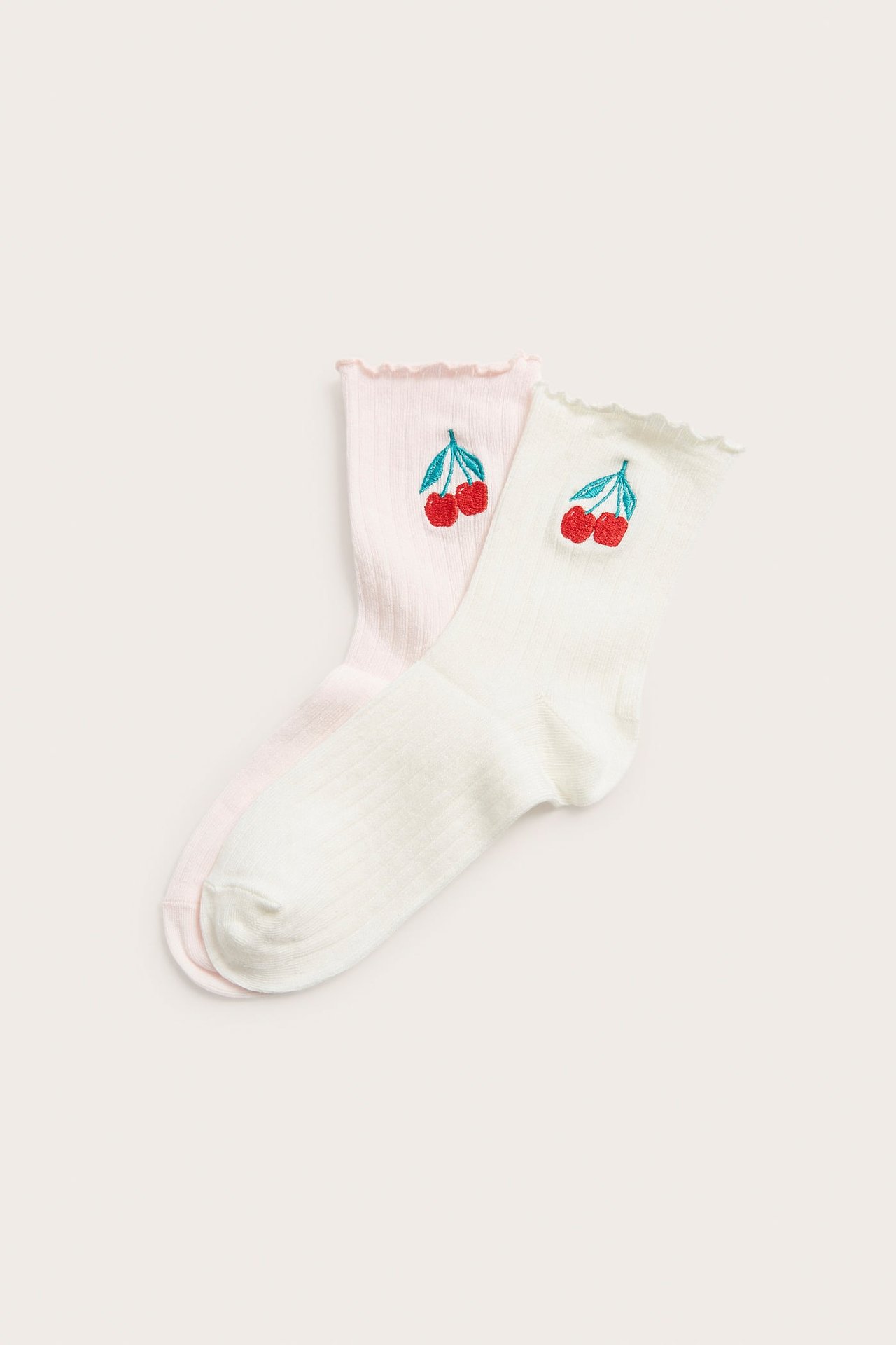 To par ribbestrikkede sokker, en rosa, en off-white, med rysjekant og broderte kirsebær.