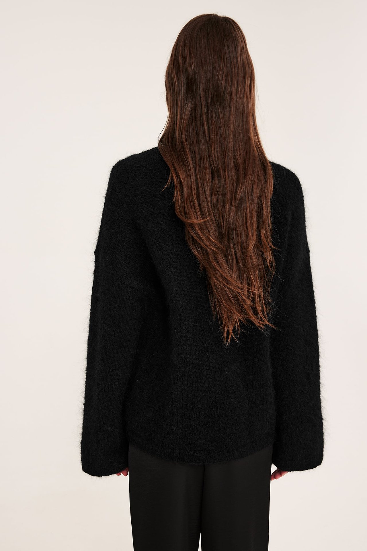 Bakifrån: Svart, fluffig oversized damtröja med svarta byxor.