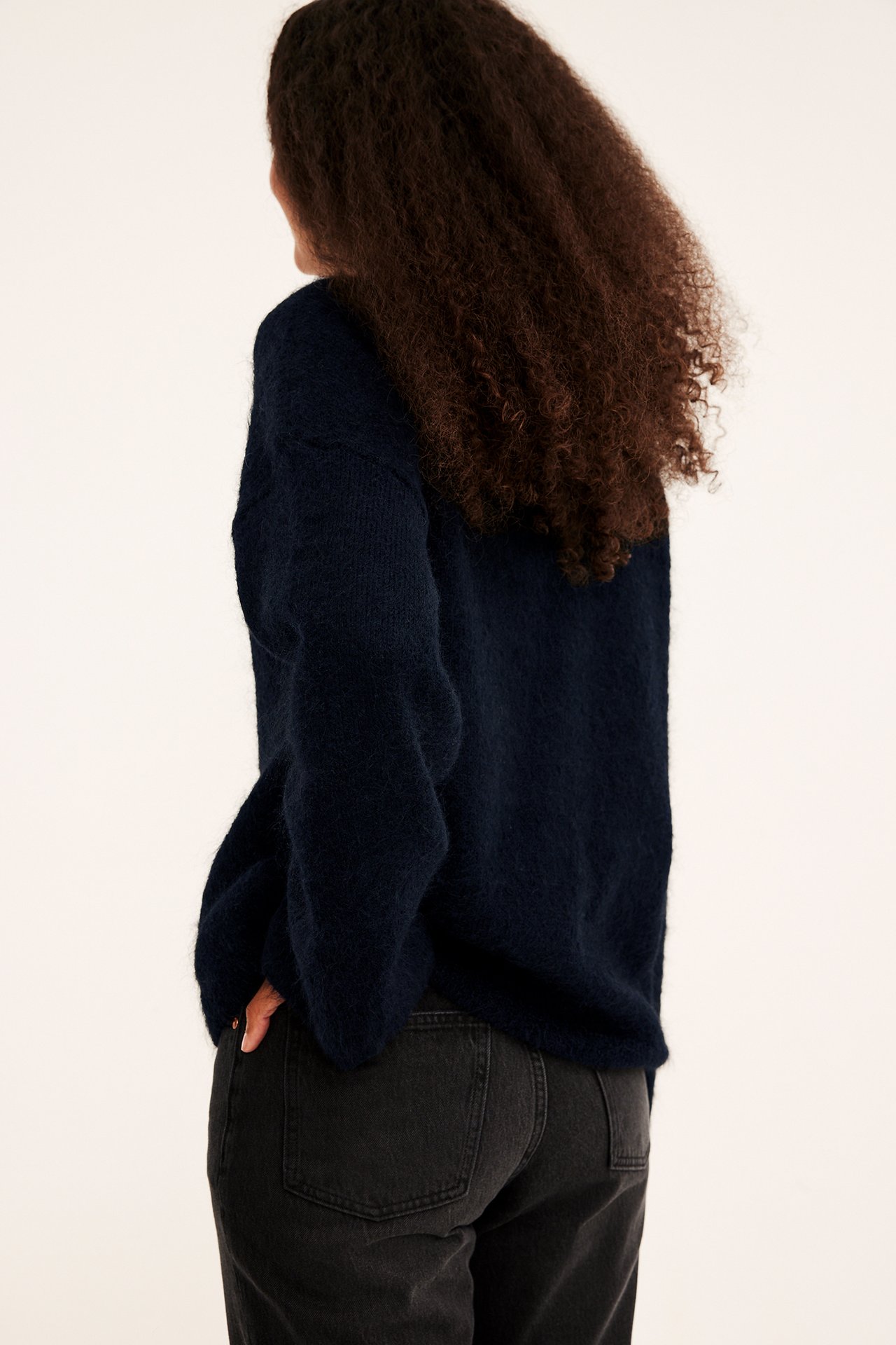 Kvinnens rygg og side i en marineblå lodden genser og mørkegrå jeans.