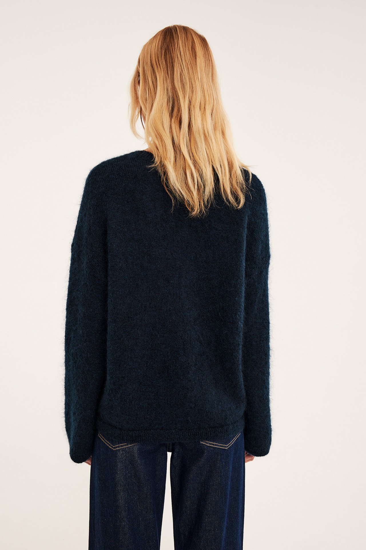 Kvinna bakifrån i mörkblå luddig stickad tröja och mörkblå jeans.