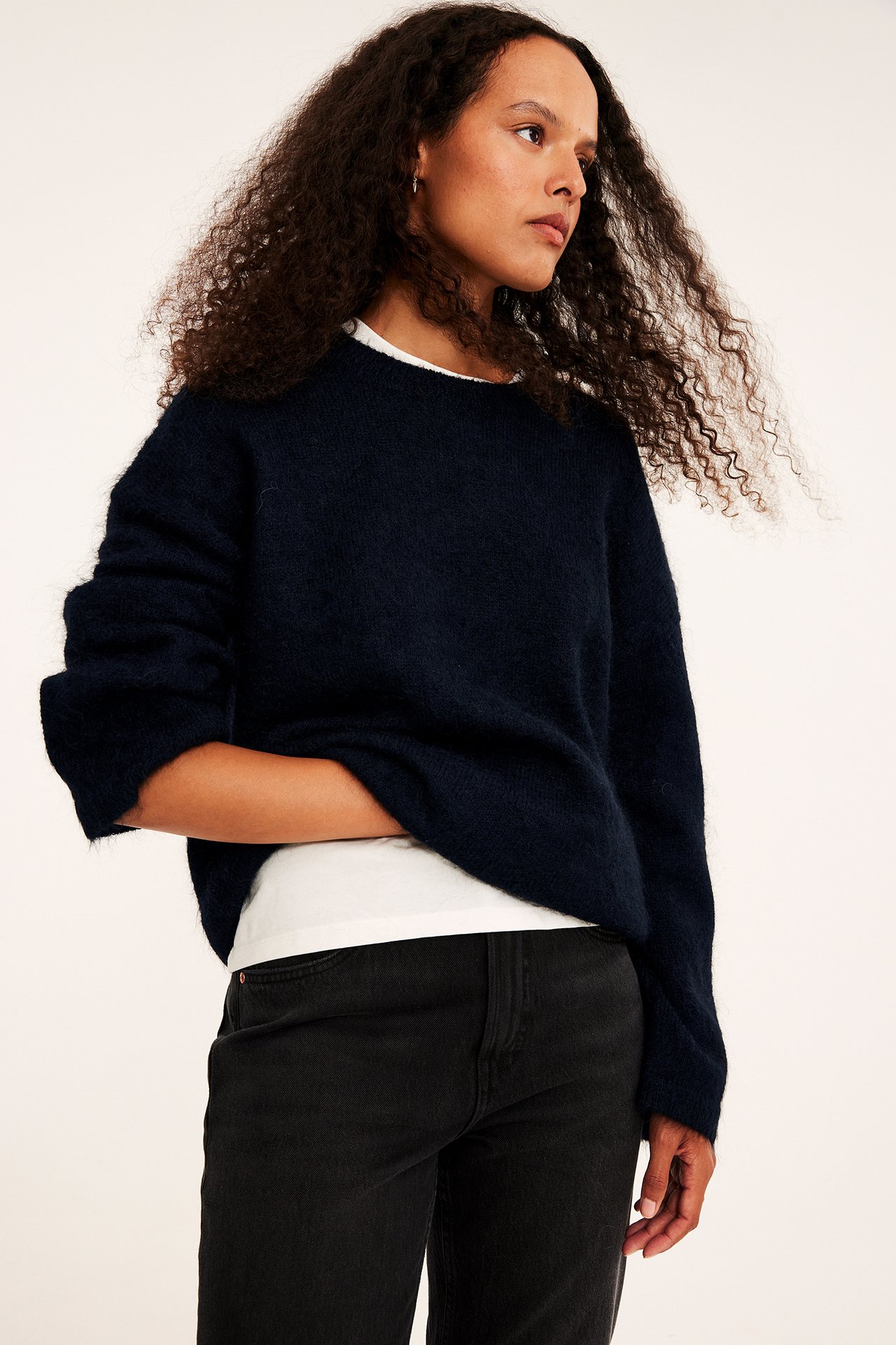 Frontbilde av kvinne i marineblå lodden oversized genser, hvit t-skjorte og svarte jeans.