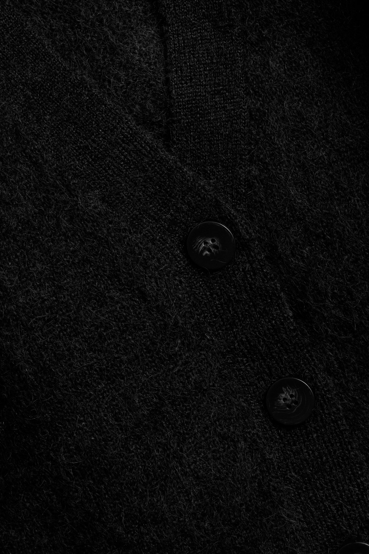Nærbilde av svart lodden strikket cardigan med to mørke knapper.