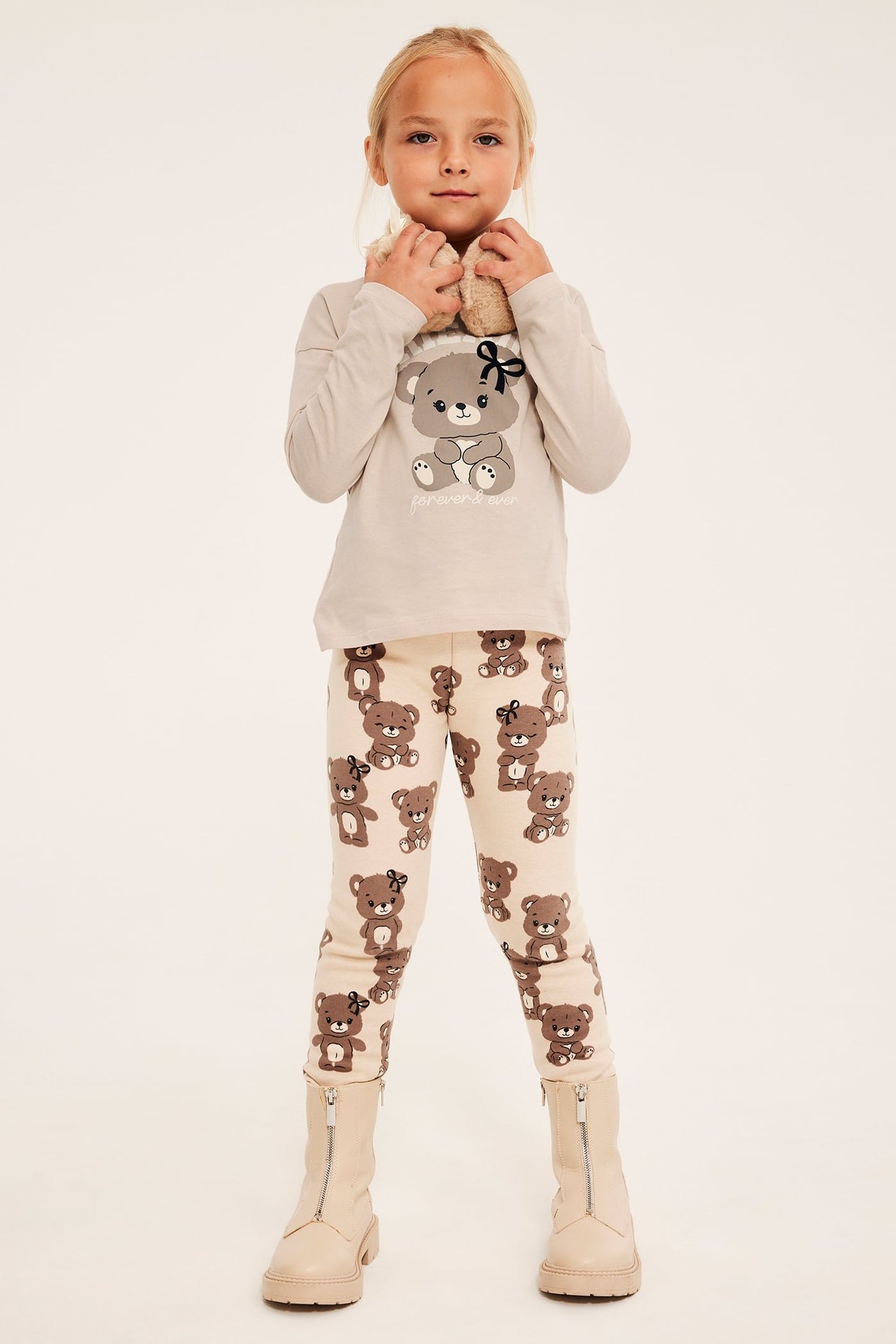 Front view: Barnets beige långärmade t-shirt med björngrafik, beige leggings med björntryck och beige kängor.