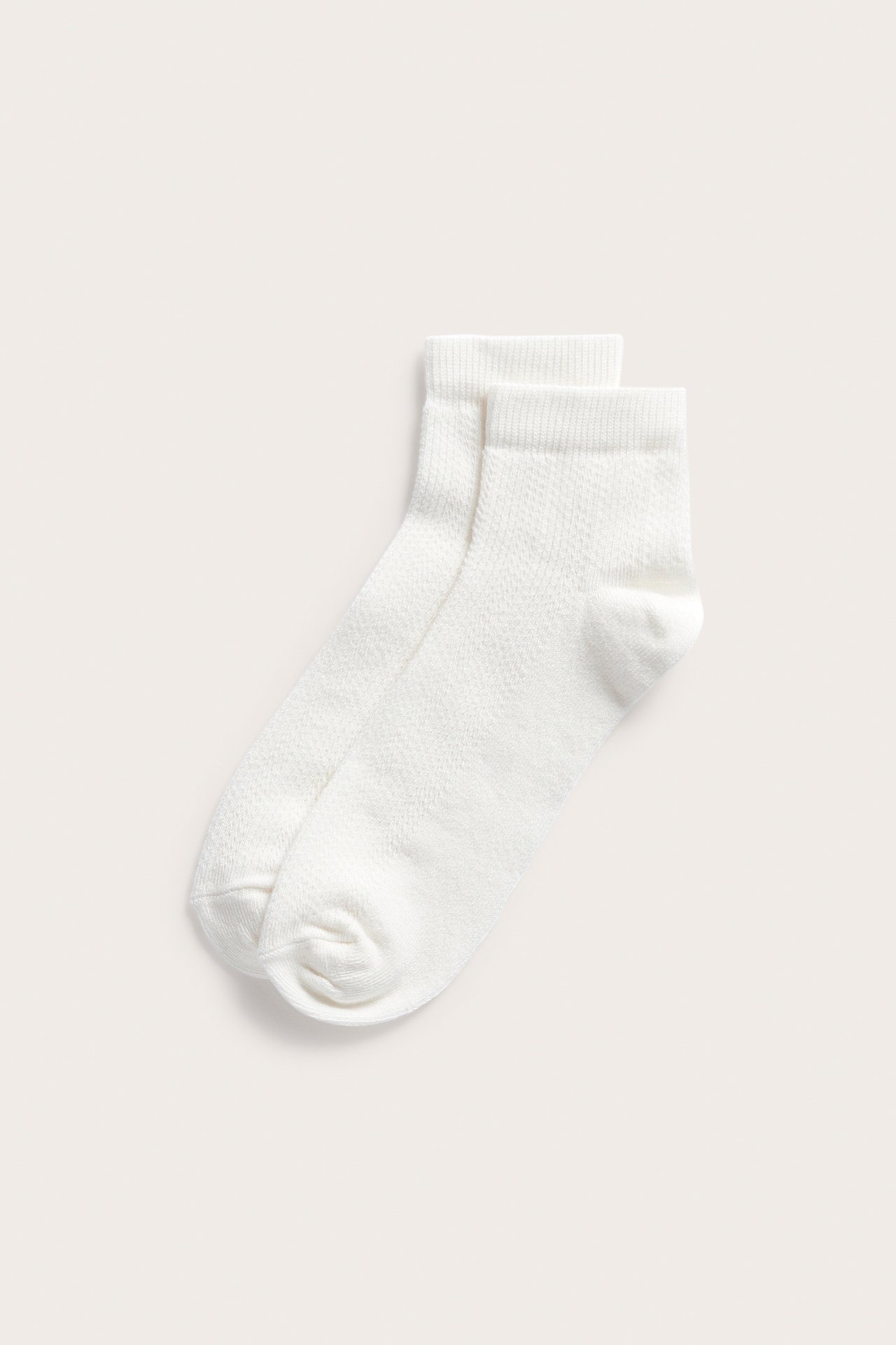 Widok z góry na parę kremowych skarpetek za kostkę we wzór pointelle.