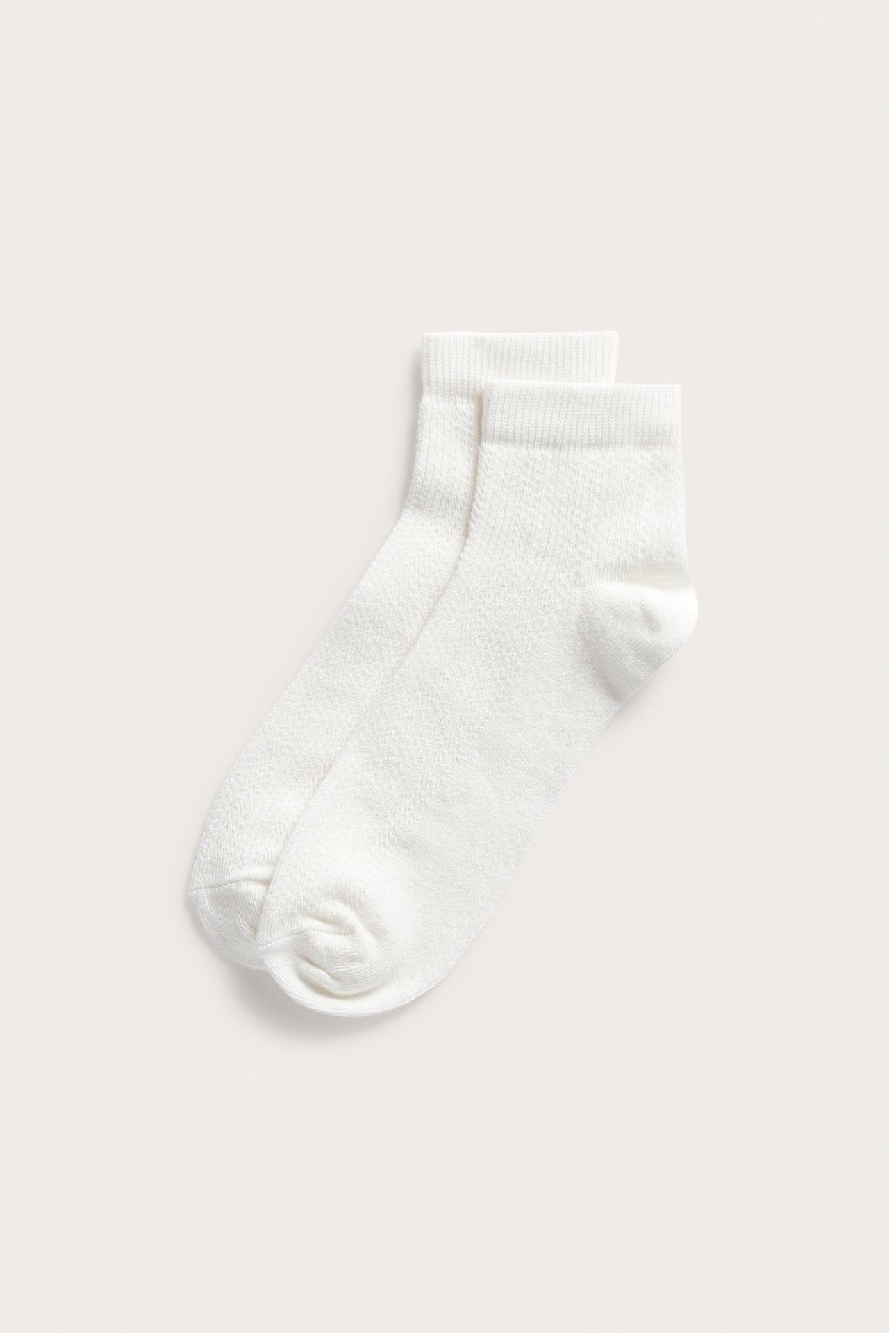 Topputsikt over et par off-white pointellemønstrede ankelstrømper.