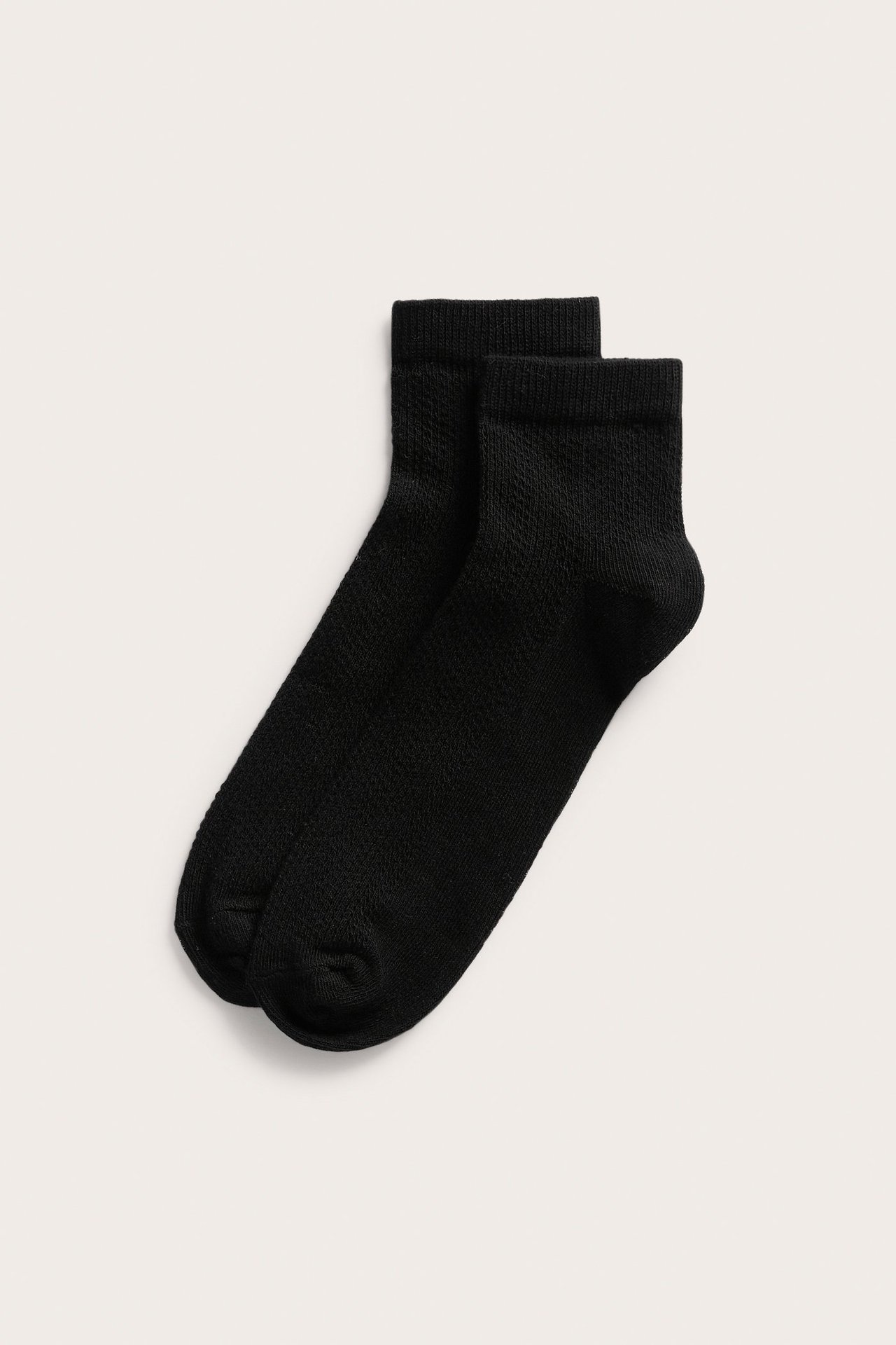 Forfra, to svarte ankelstrømper med pointellemønster lagt flatt.