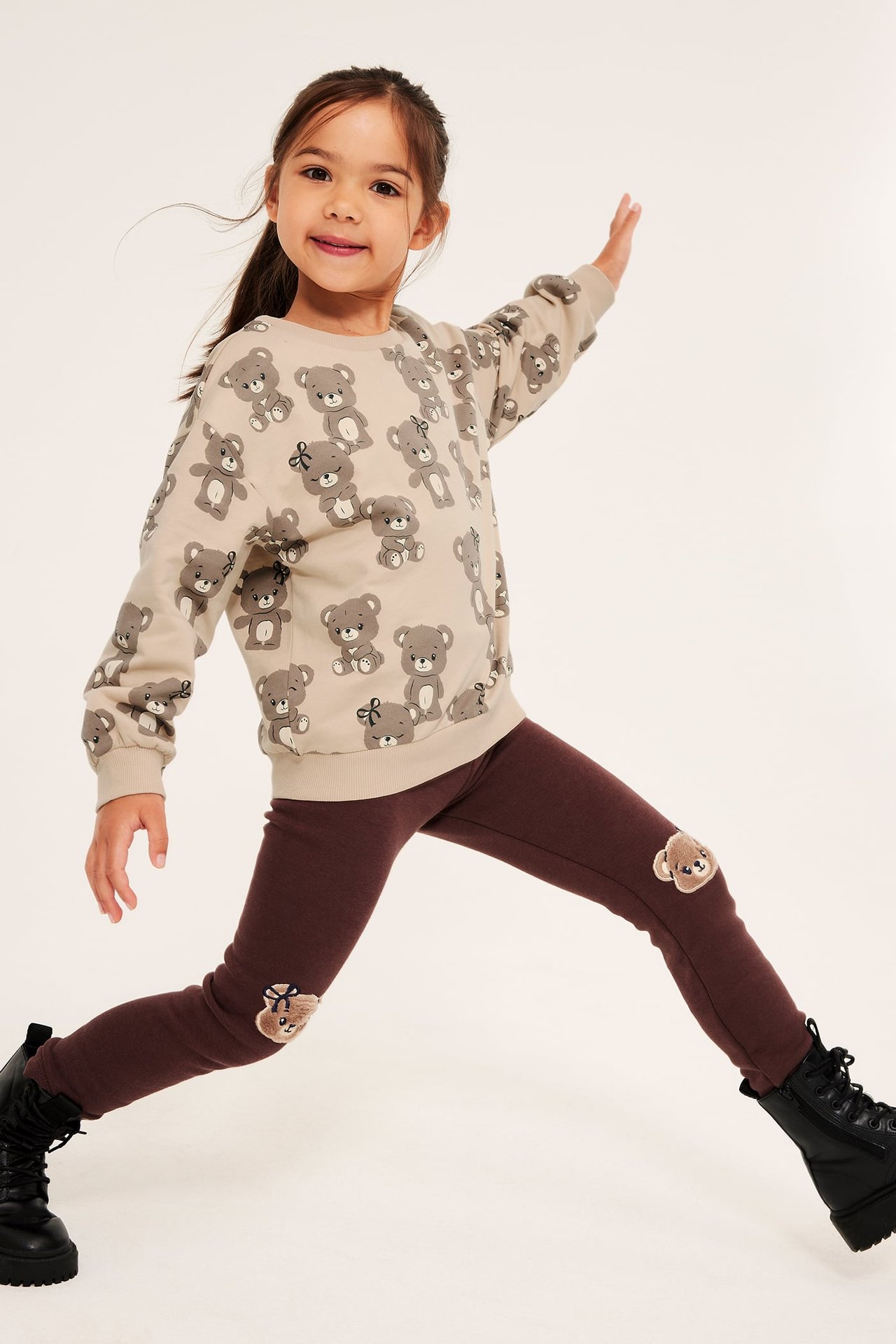 Frontbilde av et barn i beige genser med bamsemønster og brune leggings med bamselapper.