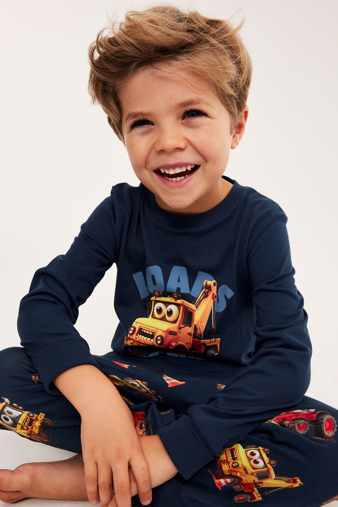 Frontbilde av et smilende barn i mørkeblått pysjamassett med byggefartøymønster.