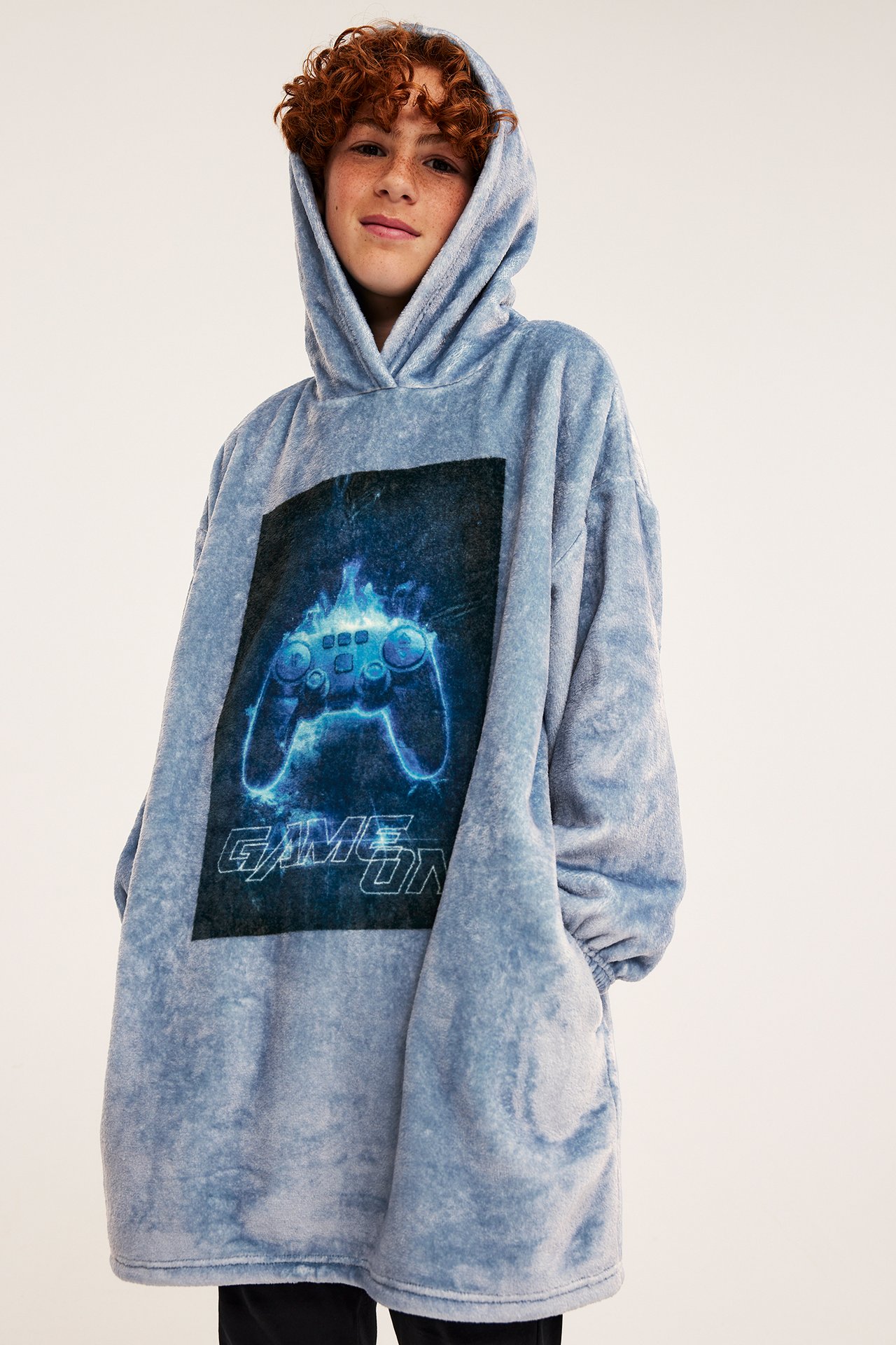 Forfra: Barn i en overdimensjonert støvblå plysjhettegenser med trykt glødende spillkontroller.