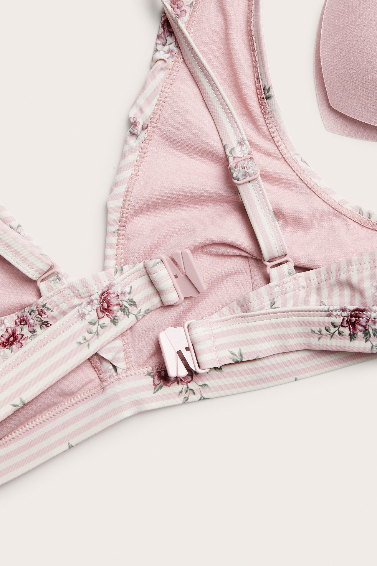 Zbliżenie różowo-białego biustonosza bikini w paski z kwiatami, różowym zapięciem i regulowanymi ramiączkami.