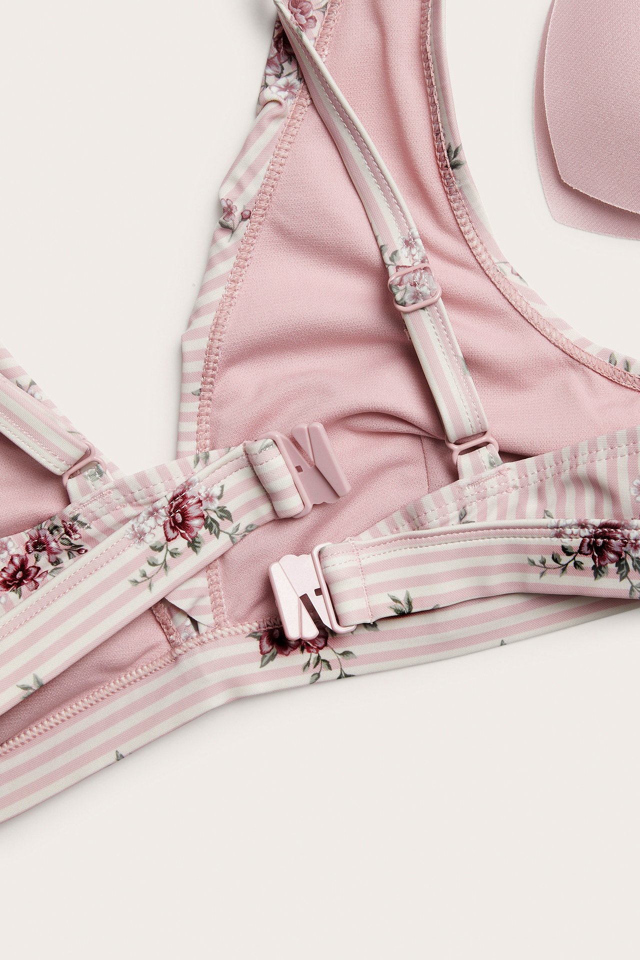 Närbild av en rosa och vitrandig blommig bikinitopp med justerbara axelband.