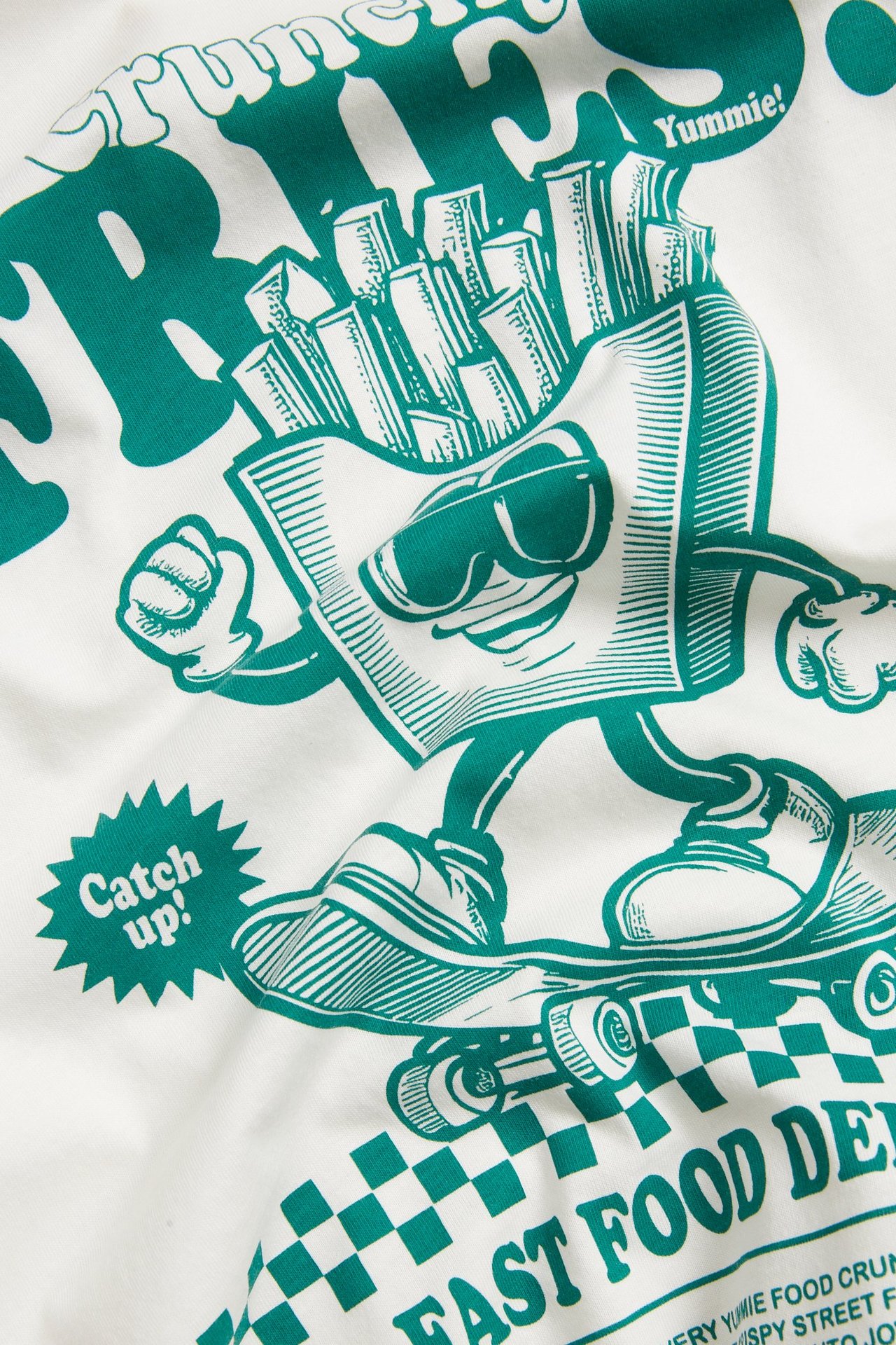 Zbliżenie na bawełnianą koszulkę w kolorze ecru z zielonym nadrukiem postaci frytek na deskorolce.