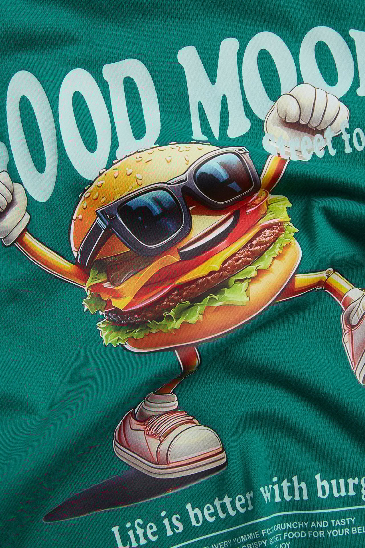 Zbliżenie na zielony bawełniany T-shirt dziecięcy z dużym nadrukiem burgera w okularach przeciwsłonecznych.