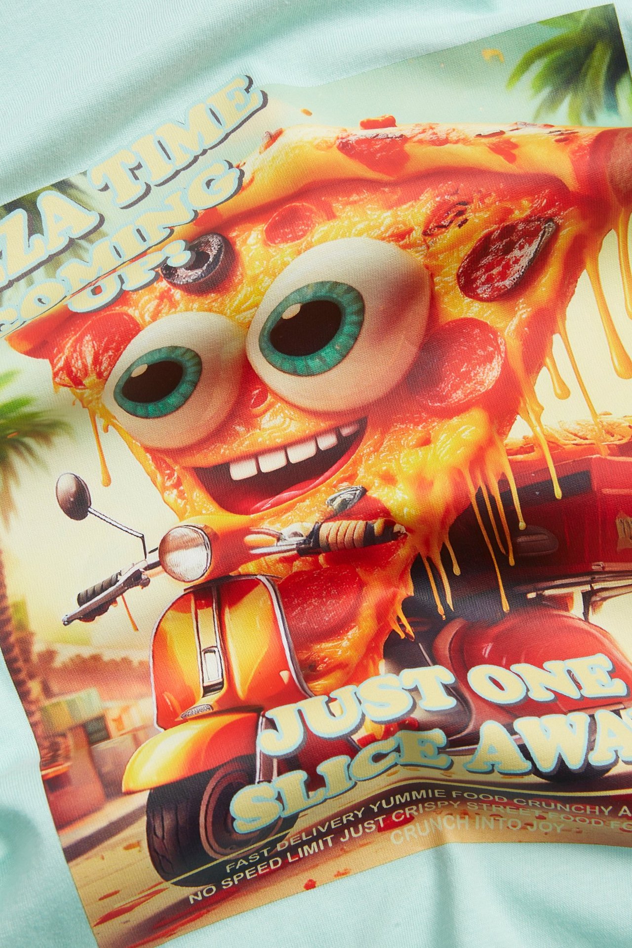 Närbild på en ljus turkos T-shirt i bomull med ett framtryck av en seriepizza på en moped.
