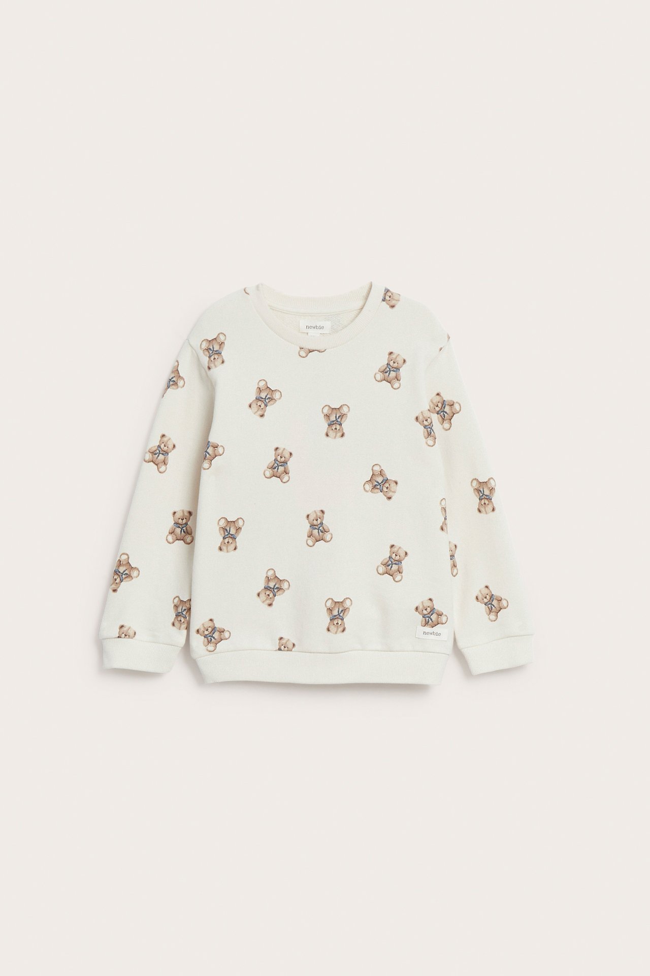 Framifrån en barnsweatshirt i ljusbeige med heltäckande brunt nallebjörnsmönster.