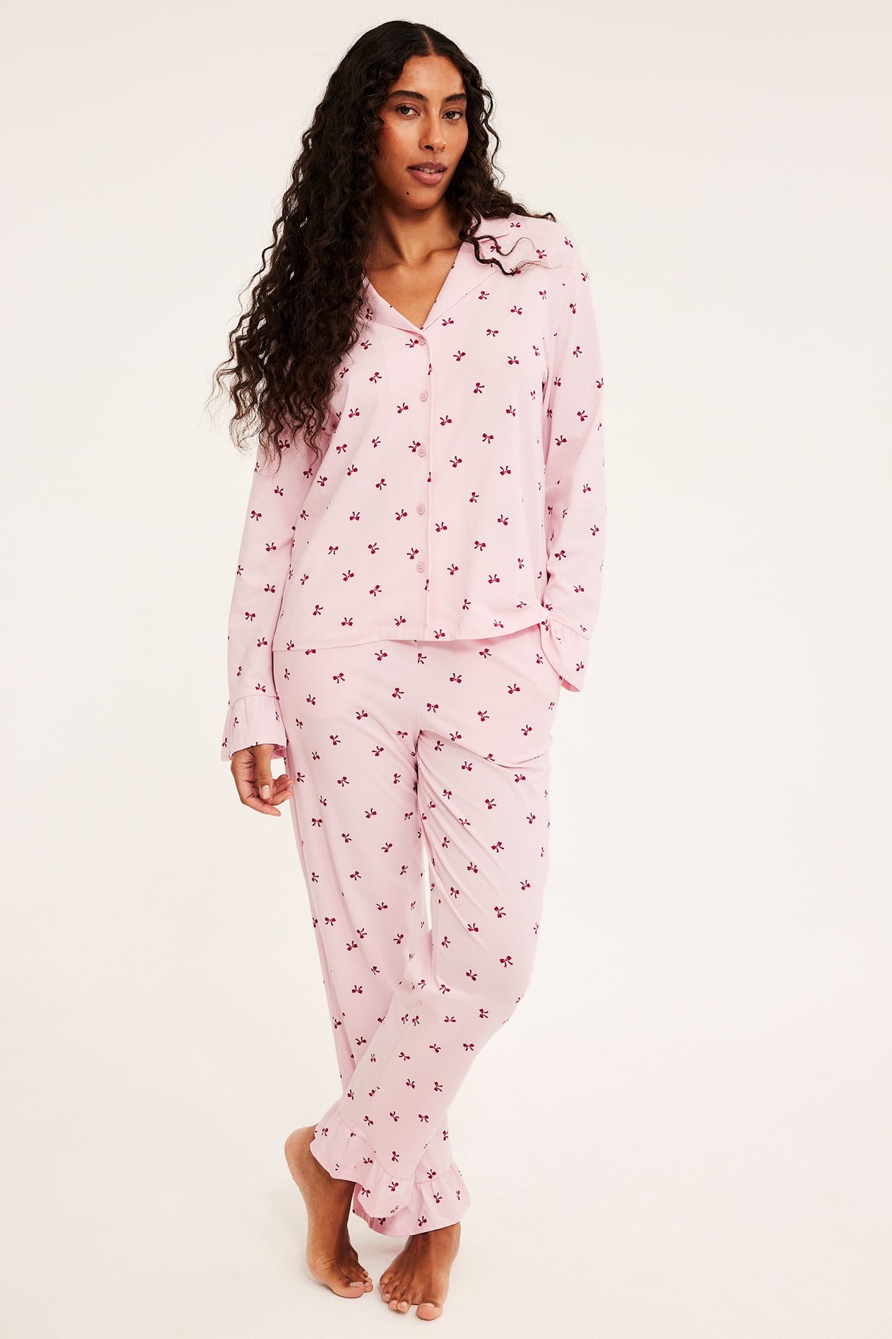 Nainen yllä: vaaleanpunainen pyjamassetti punaisilla ruseteilla, röyhelökauluksella ja hihansuilla.