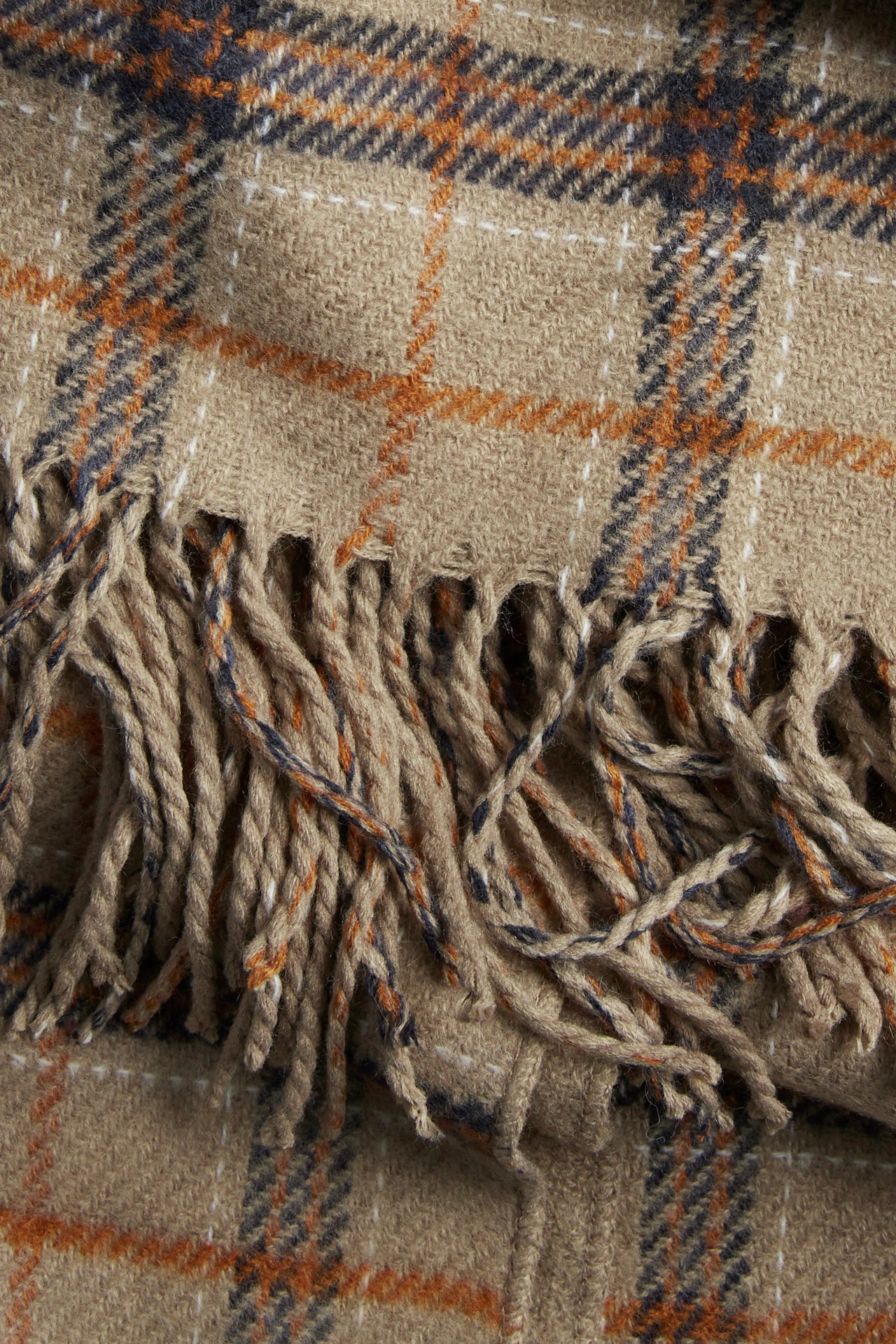 Nærbilde av et beige pledd med oransje, marineblå og hvite striper og frynser.
