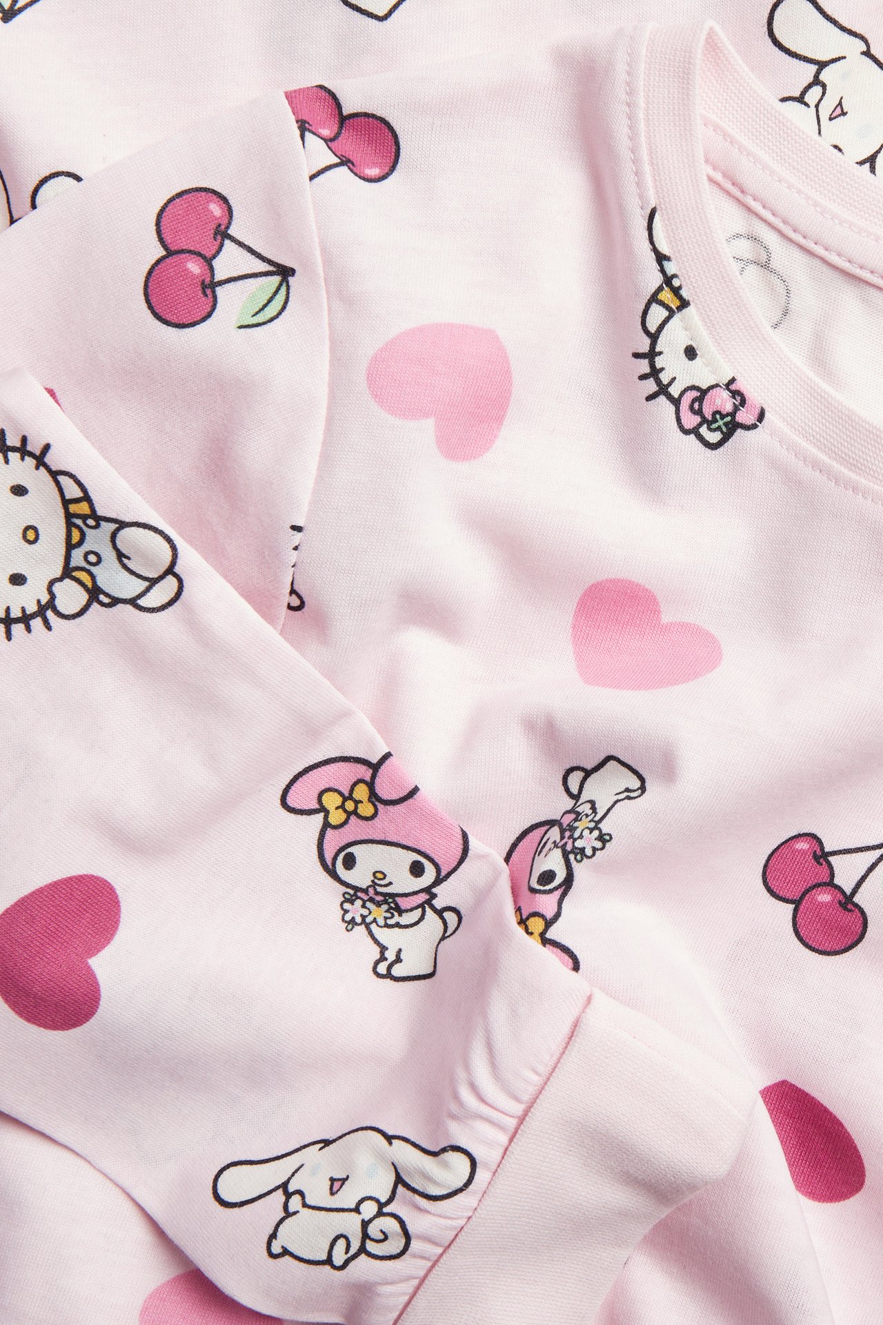 Närbild på en rosa Sanrio-pyjamastopp med karaktärstryck, hjärtan och körsbär.
