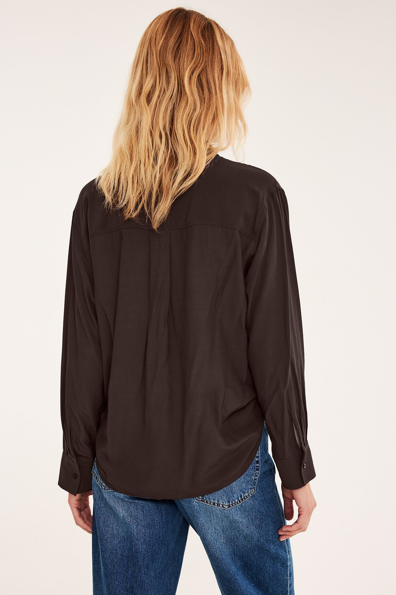 Bakifrån på en kvinnlig modell i en mörkbrun långärmad skjorta och blå jeans.